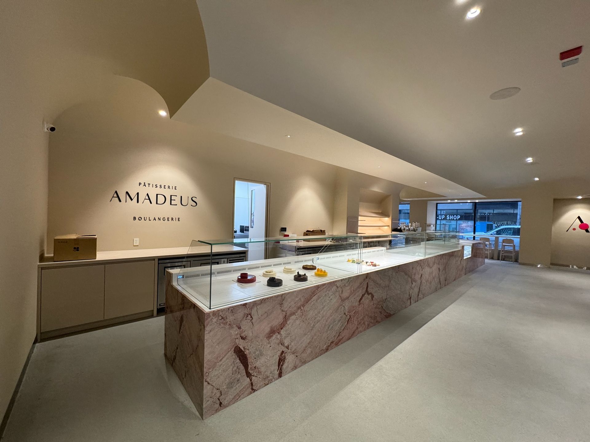 Interior of Amadelle bakery. Display case with pastries, pink marble, beige walls, and logo.