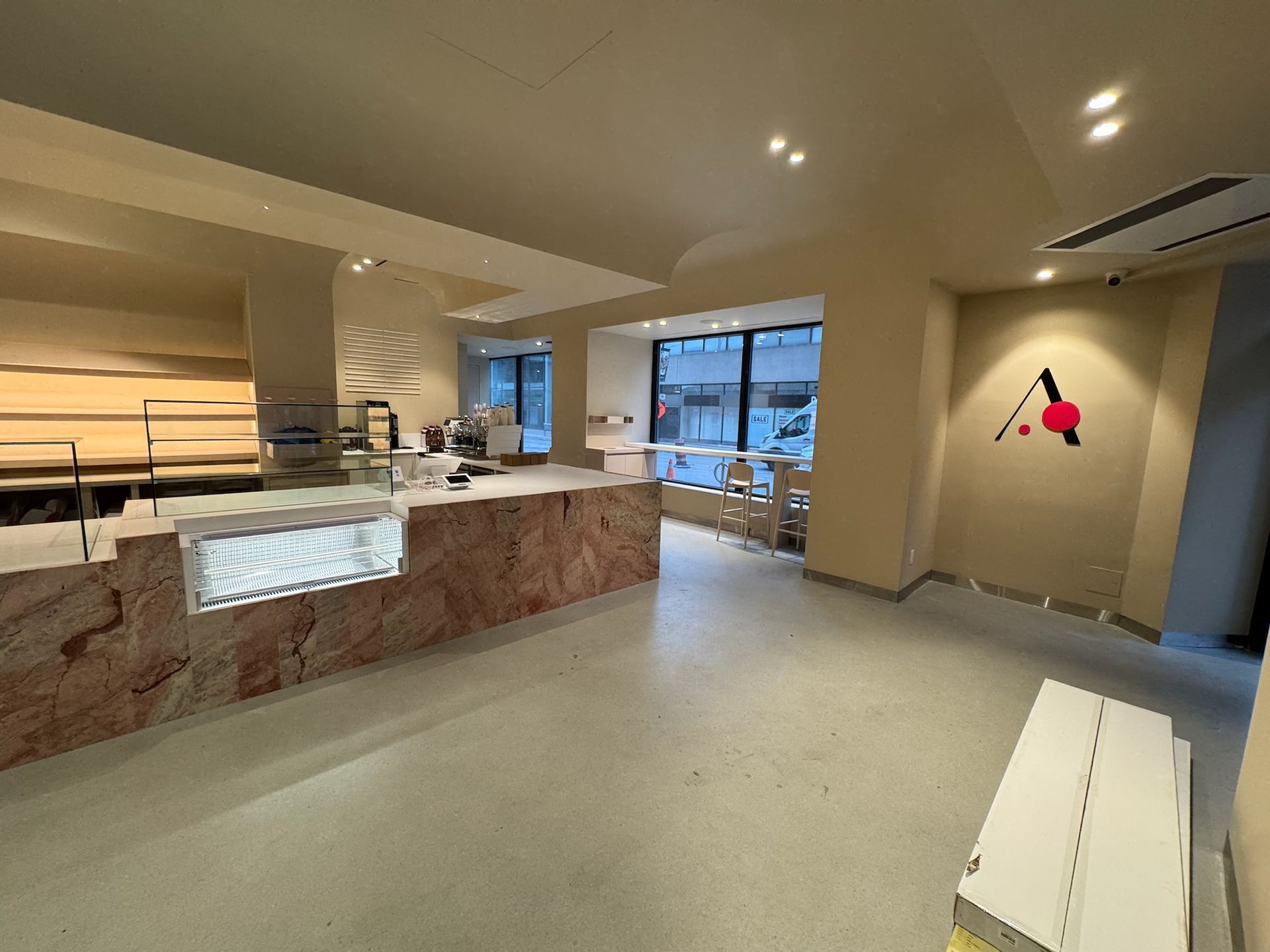 Empty cafe interior with pink counter, display cases, and logo on wall.
