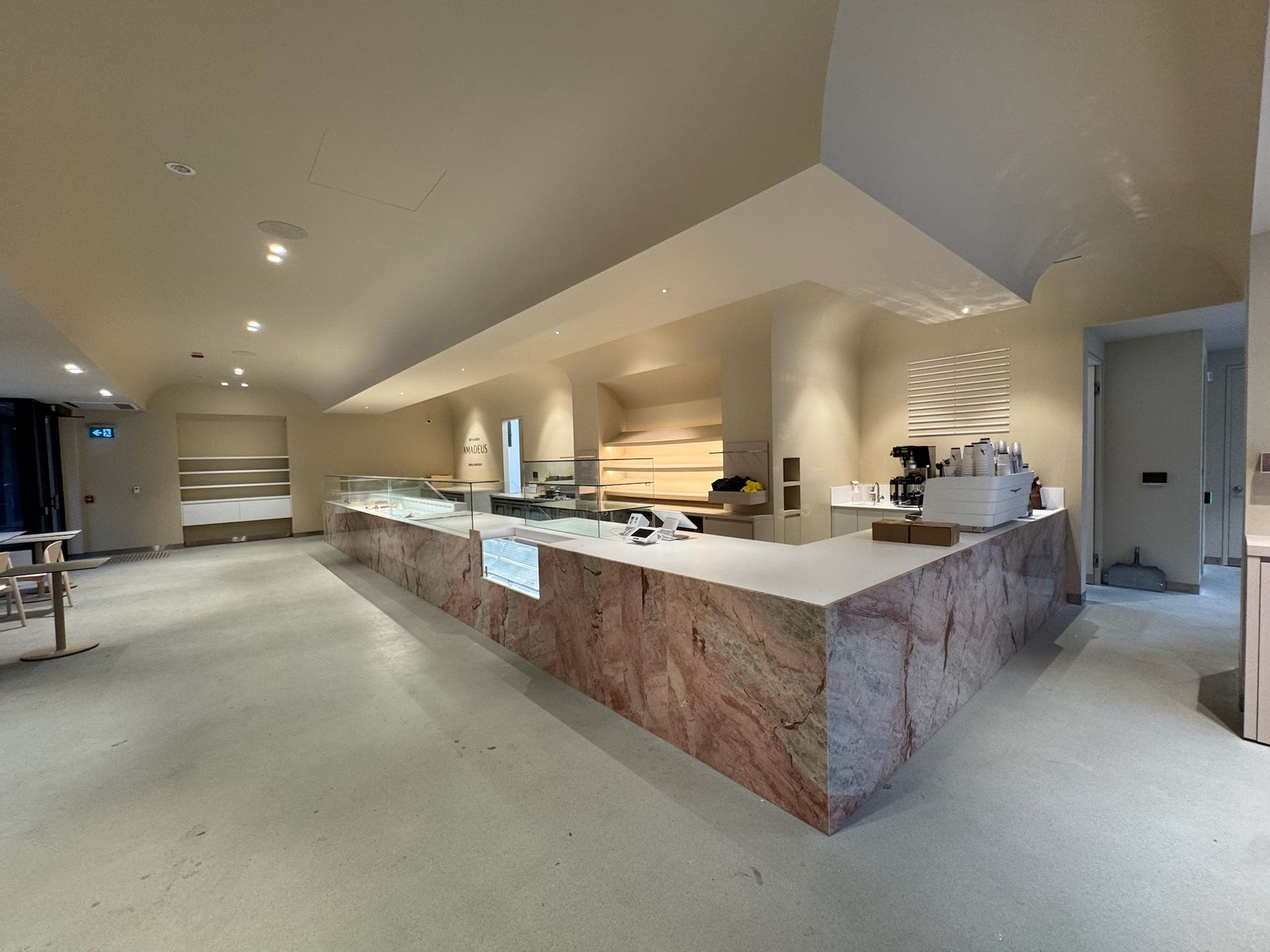 Long, pink marble counter in a modern, beige cafe. Empty space with lights and minimalist design.