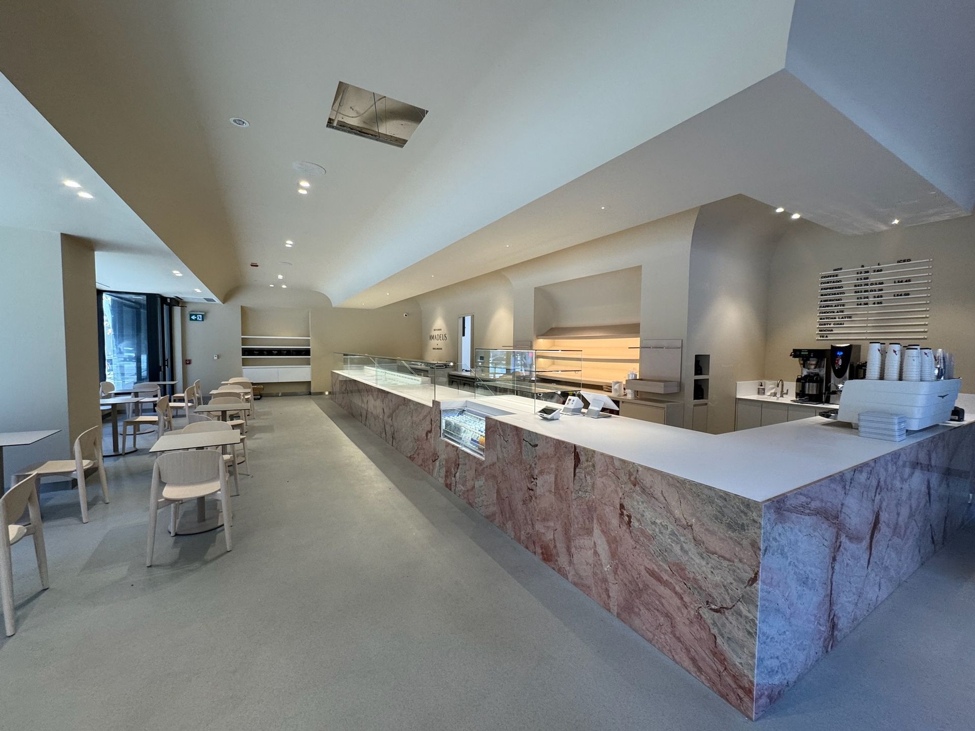 Interior of a light-colored cafe with a marble counter, tables, and a coffee machine.