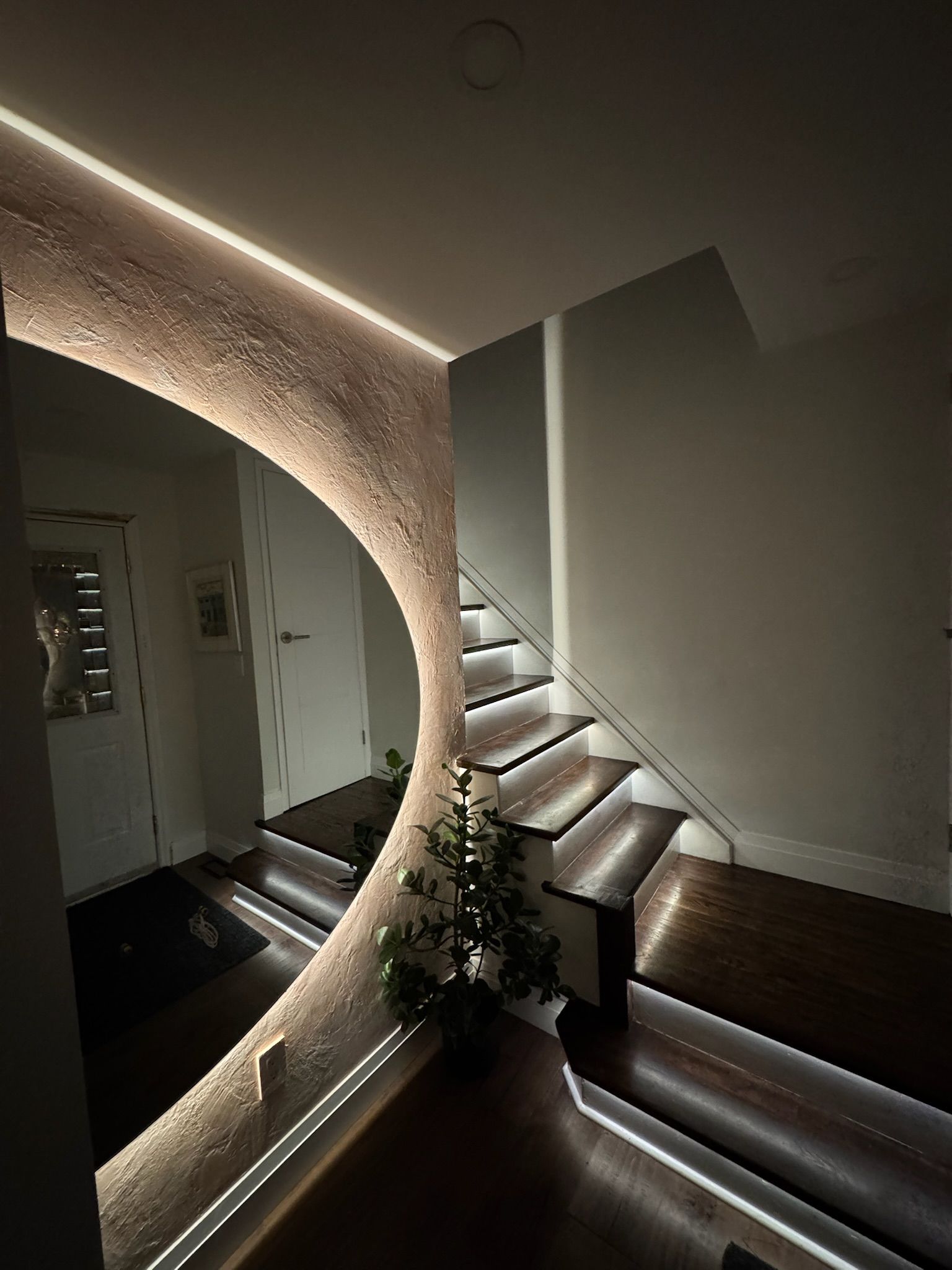 Circular mirror with LED strip lights, reflecting entry hall and staircase.