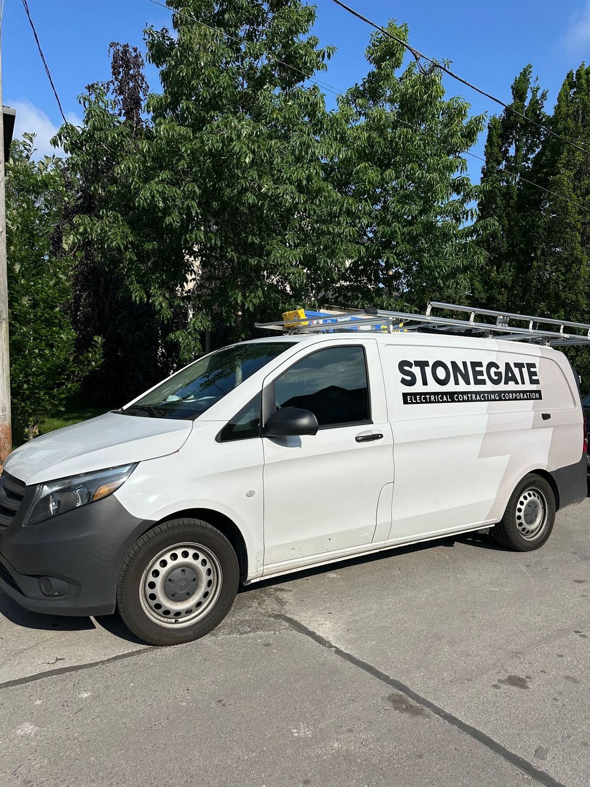 White Stonegate van parked on a street with a ladder on top, trees in the background.
