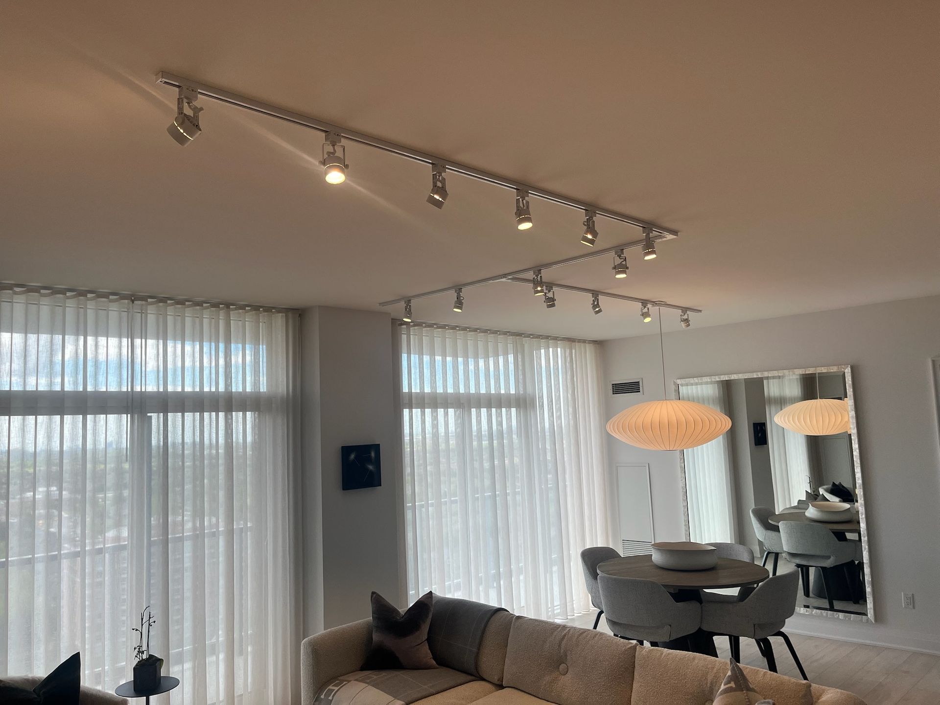 Living room with track lighting, sheer curtains, and a dining table.