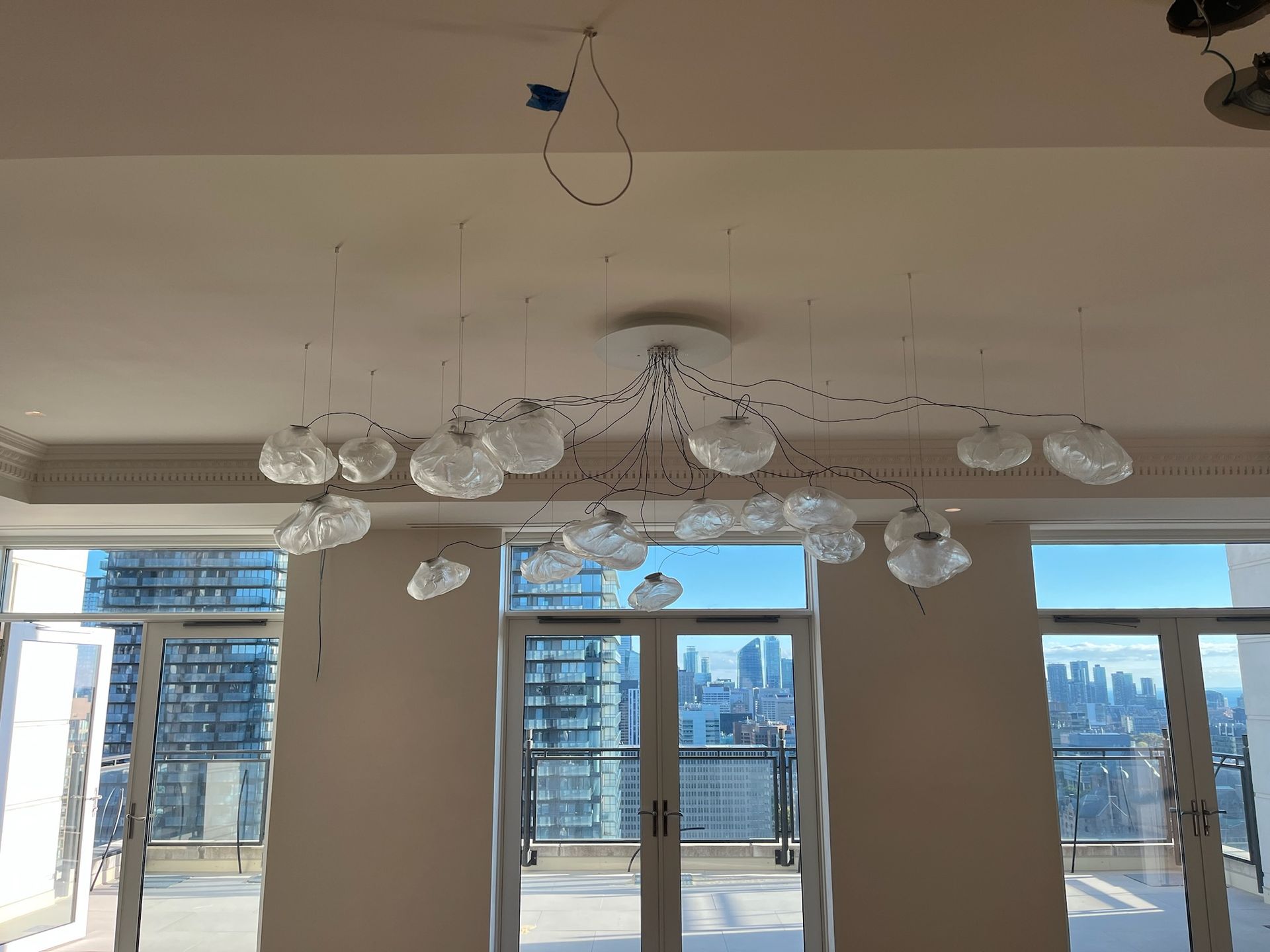 Modern chandelier with glass globes, mounted on a white ceiling in a room with a city view.