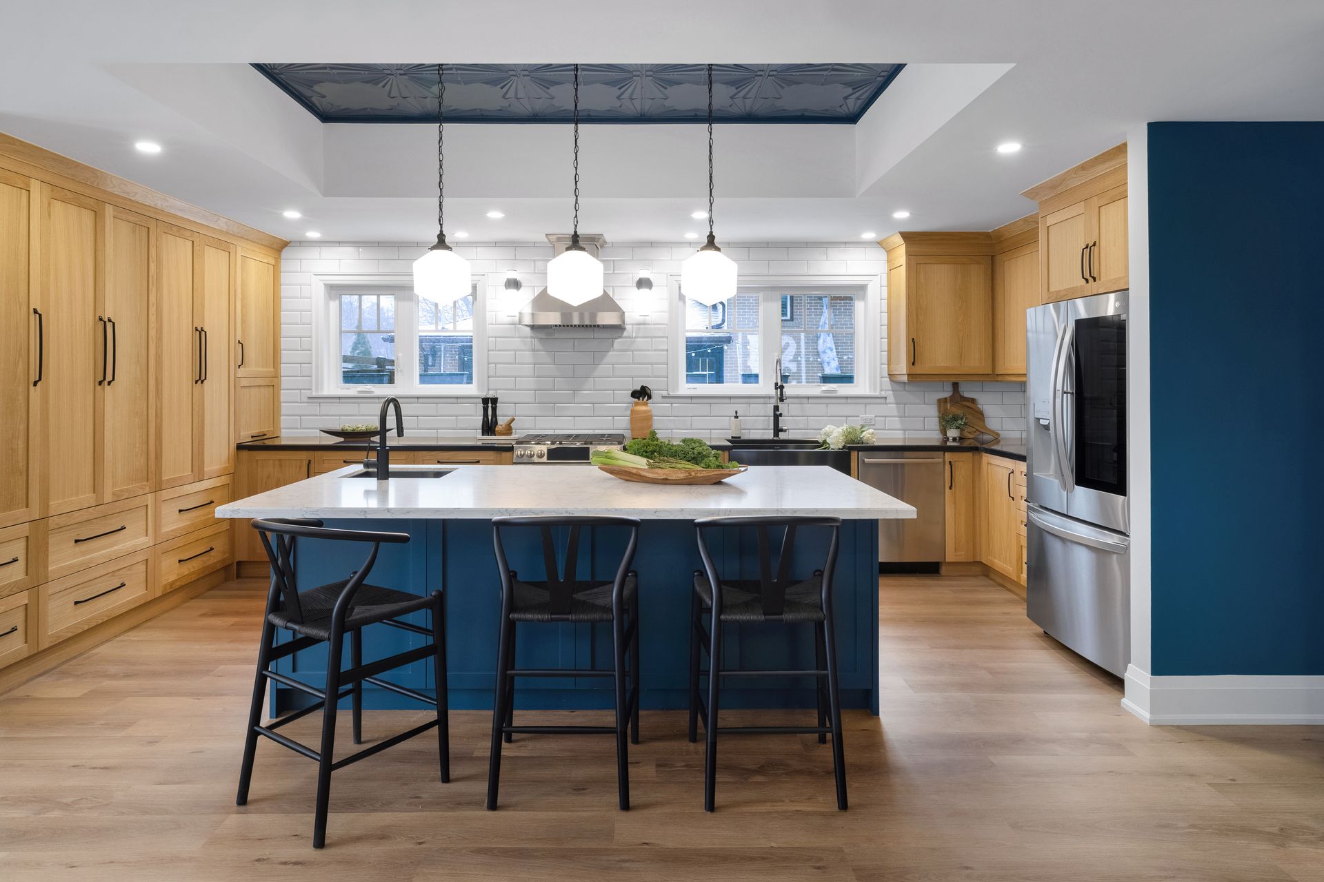 Modern kitchen with blue island, light wood cabinets, and stainless steel appliances.