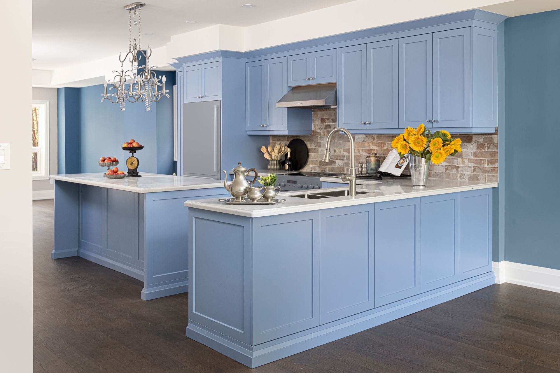 Blue kitchen with island, marble countertops, stainless steel appliances, brick backsplash.
