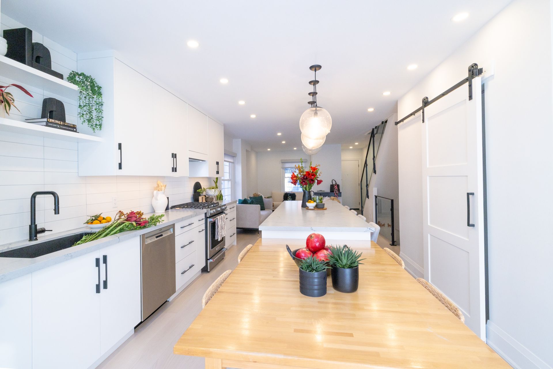 Modern white kitchen with island, stainless steel appliances, wood table, and sliding barn door.