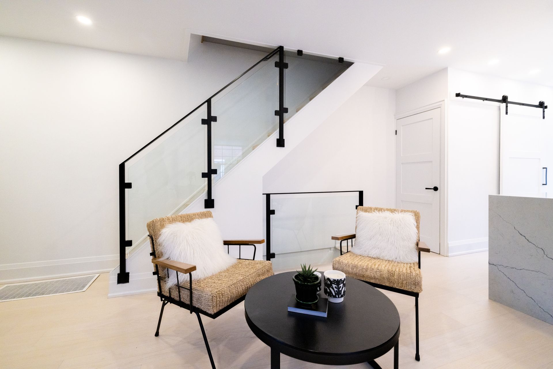 Modern living room with staircase, two chairs, and a round black coffee table.