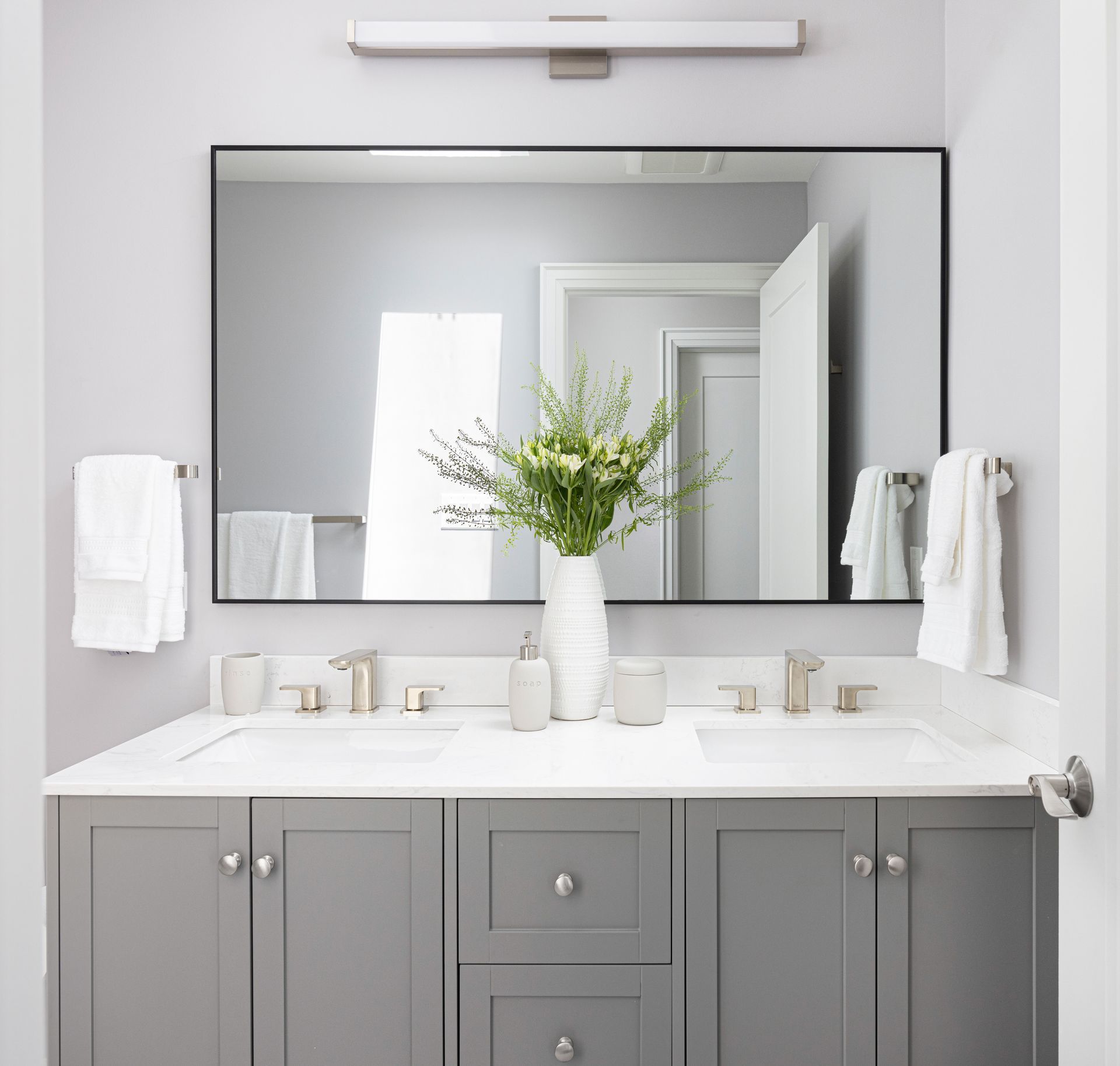 Gray bathroom vanity with double sinks, large mirror, and white towels.