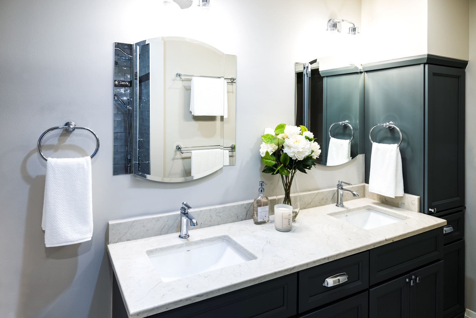 Gray bathroom with dual sinks, dark cabinetry, marble countertop, and white towels.