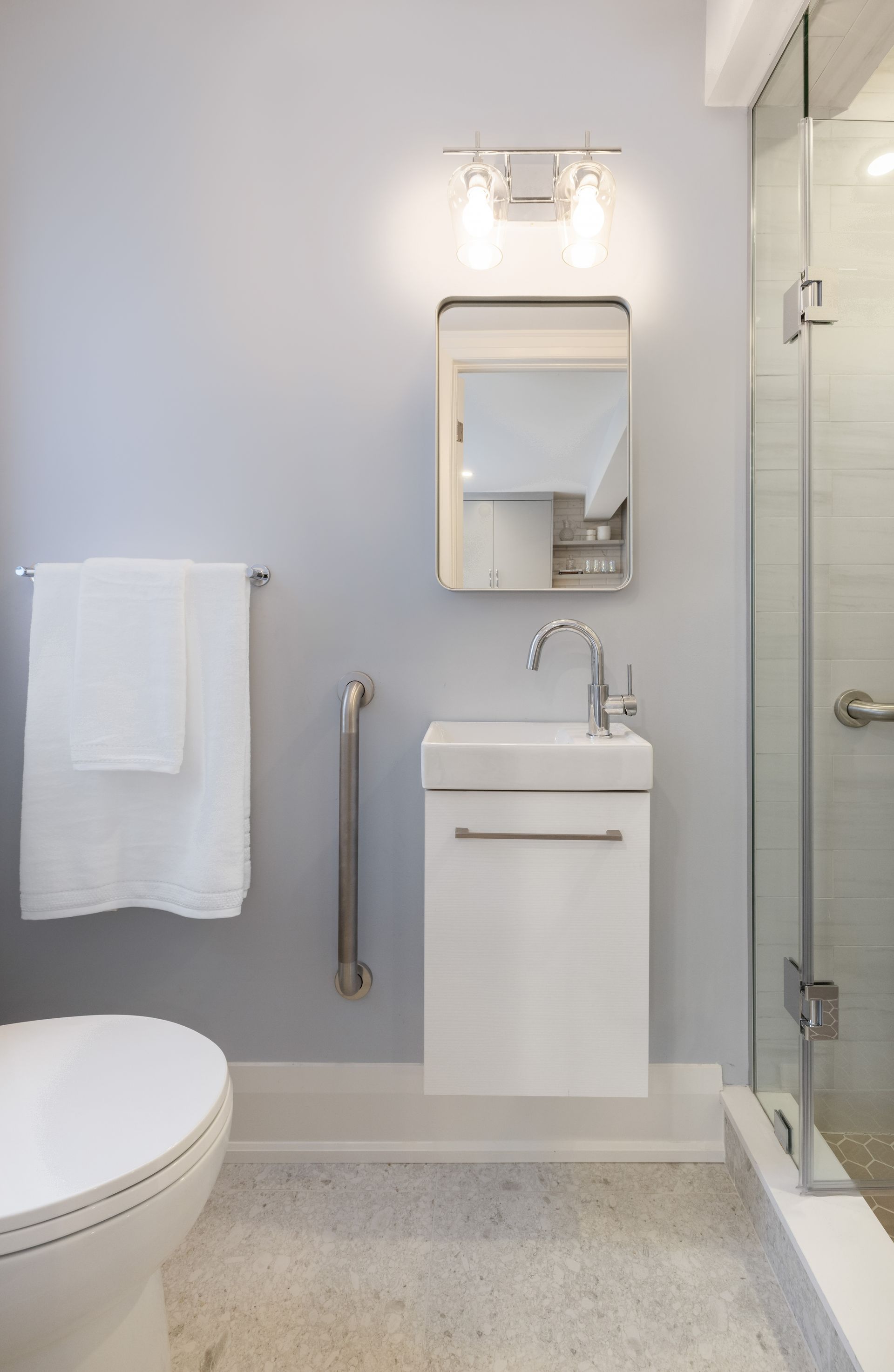 Small bathroom with accessible features. Features a toilet, sink, grab bar, and walk-in shower.