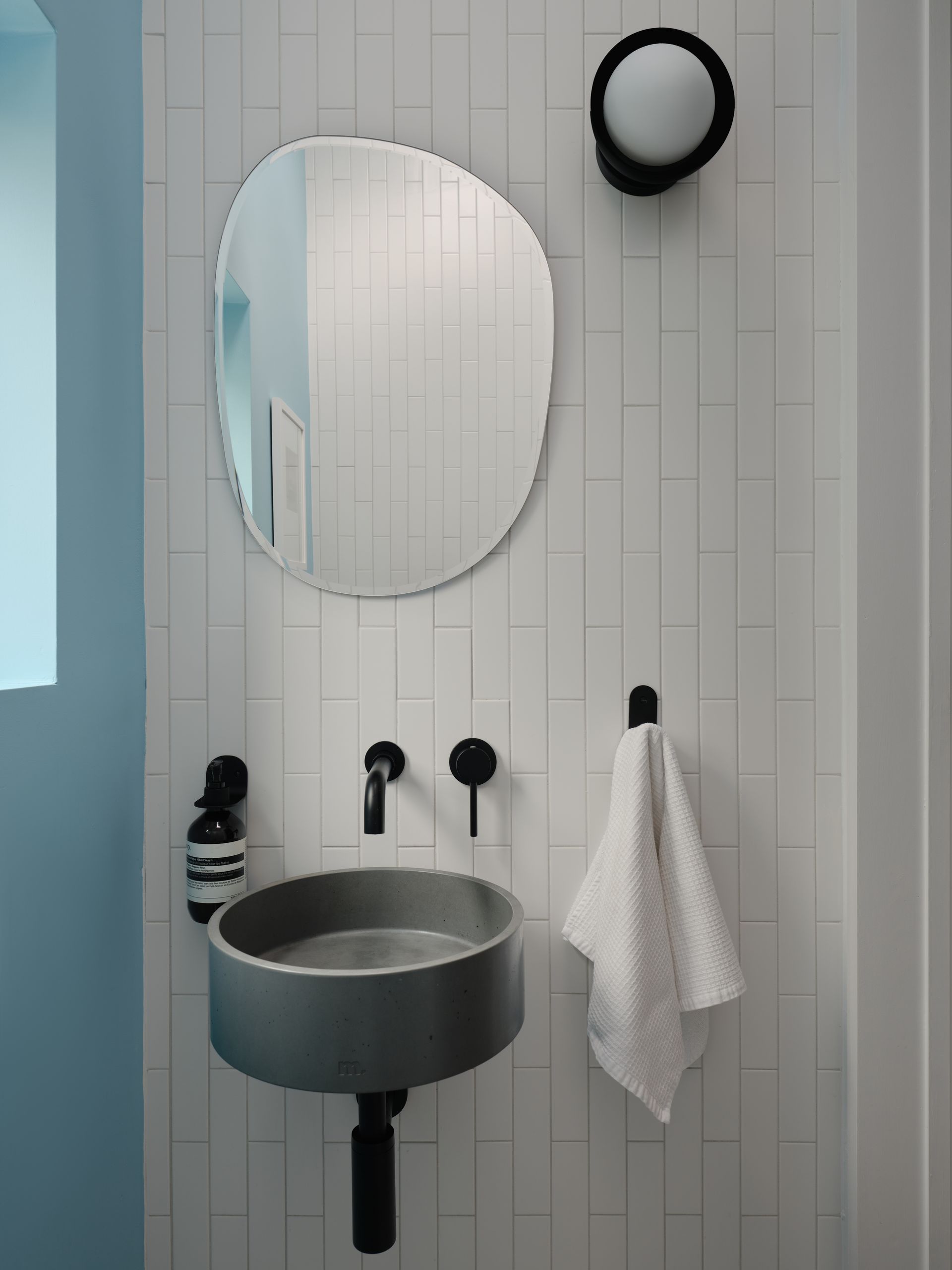 Small bathroom with gray concrete sink, black fixtures, and organic-shaped mirror.