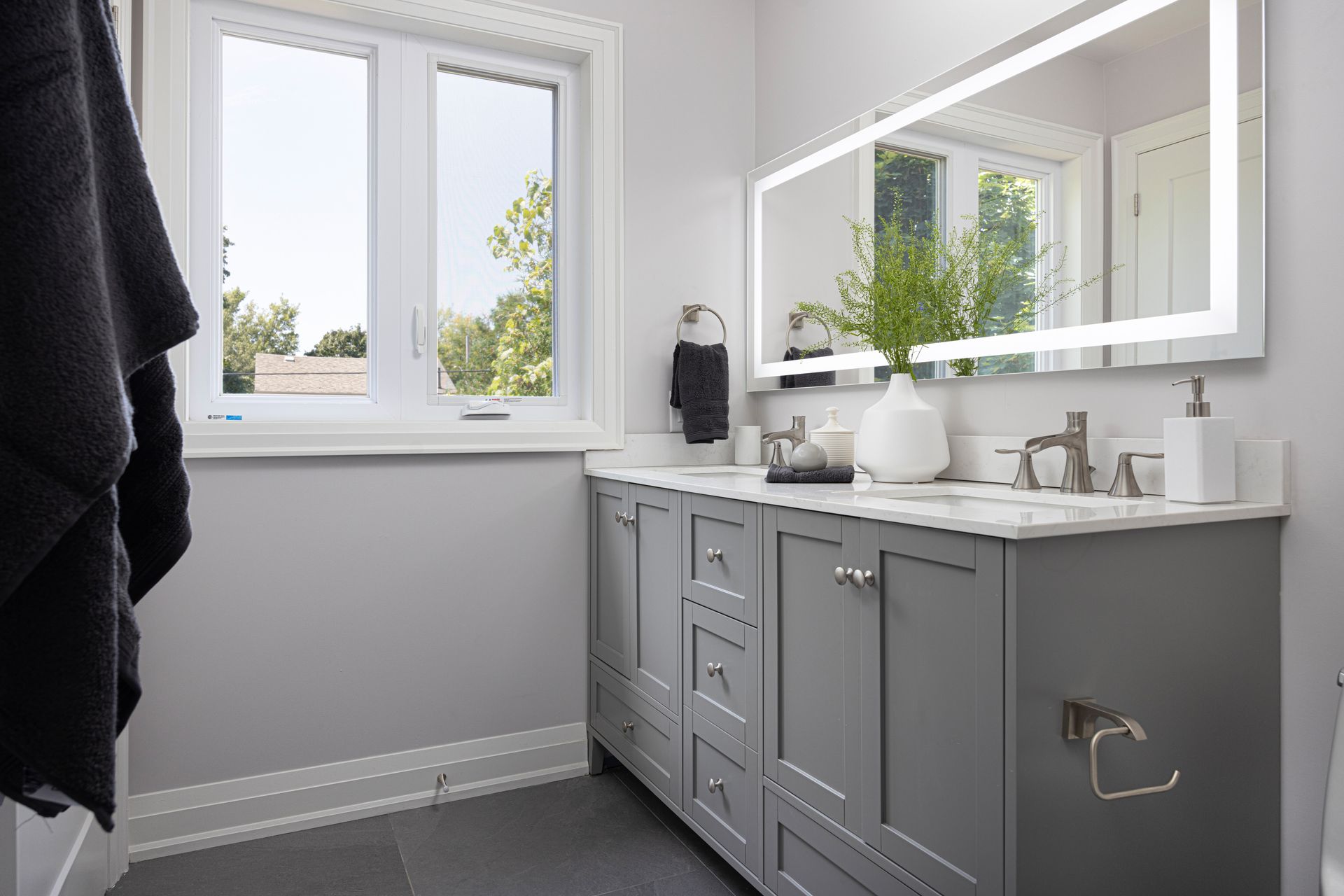Gray bathroom with vanity, window, mirror, and towel.