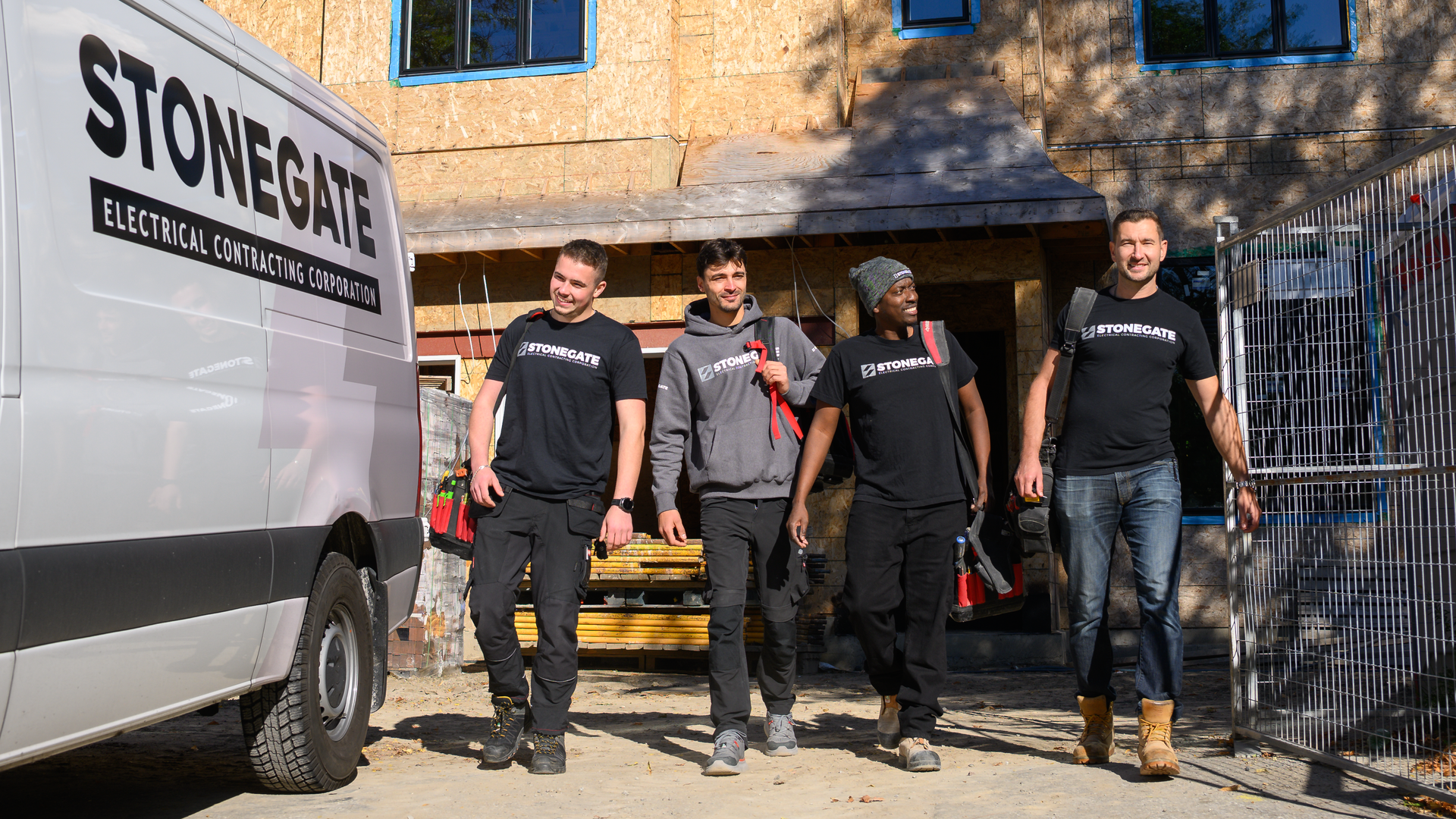 Four people in t-shirts walk from a Stonegate Electrical van towards a building under construction.