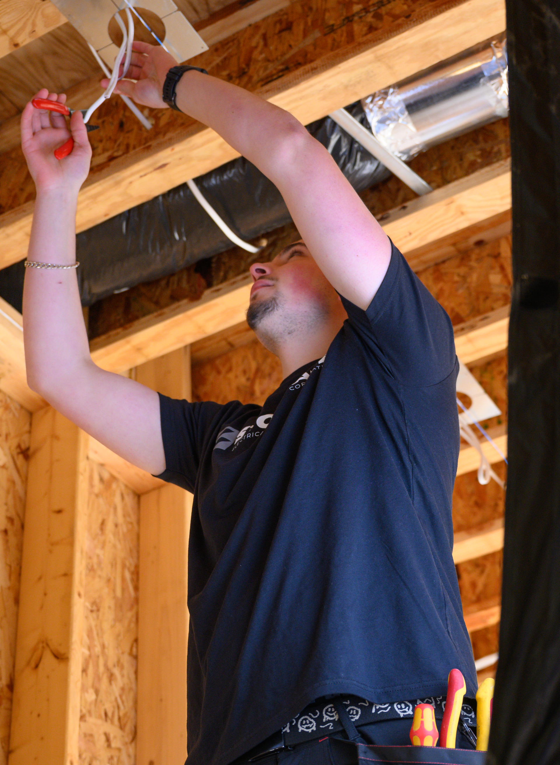 Electrician working on wiring in a wooden framed ceiling.