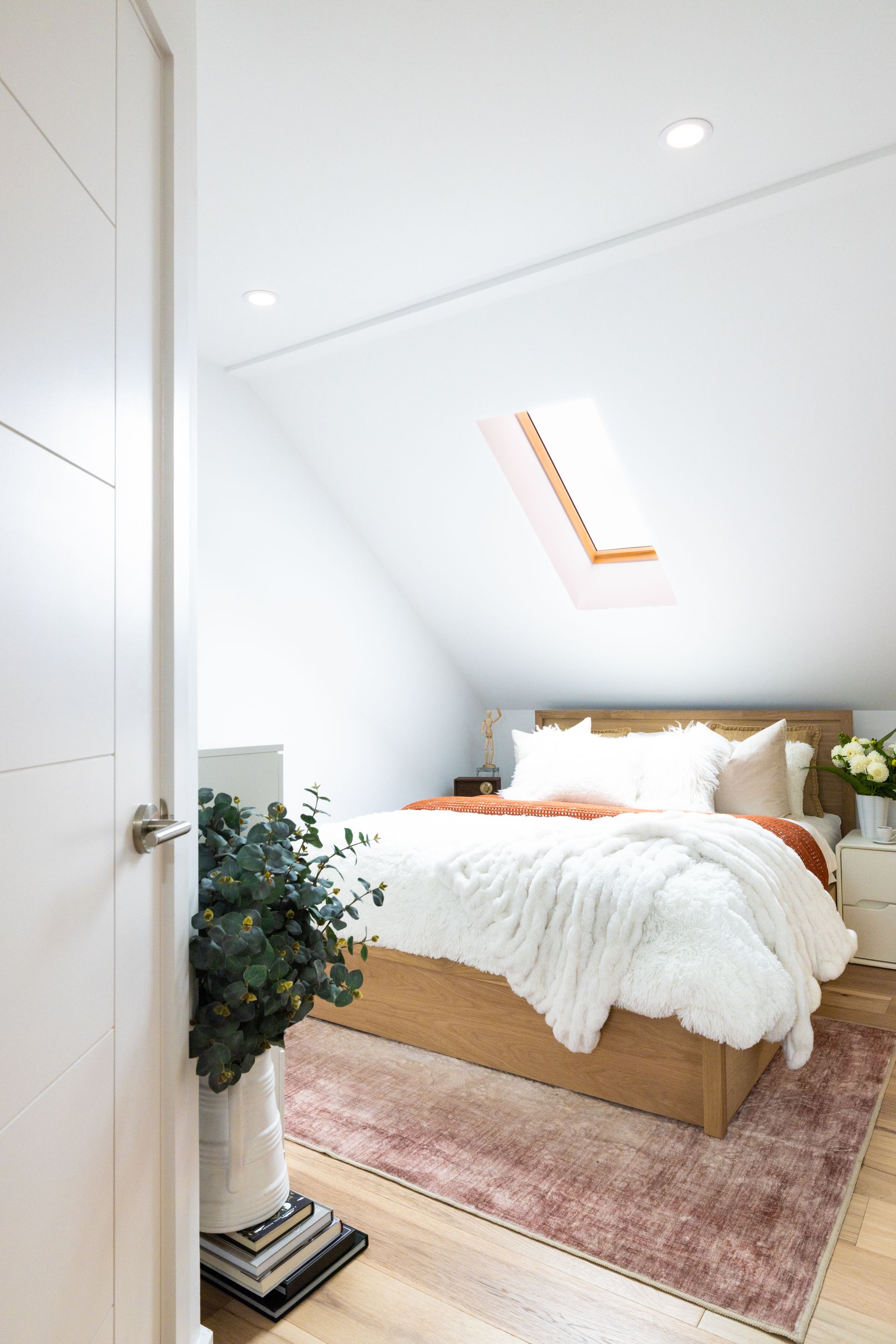 Bedroom with wooden bed, white bedding, and a skylight in a slanted ceiling.