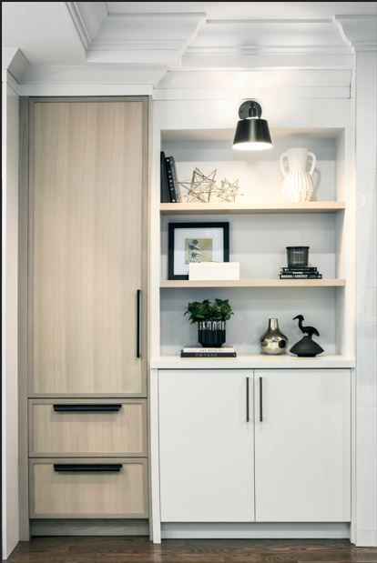 Built-in storage unit with light wood cabinets, white shelves, and decor, illuminated by a black sconce.