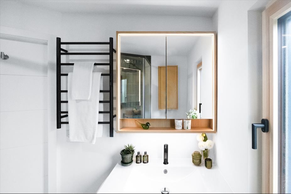 Modern bathroom with black towel rack, lighted mirror, and white sink.