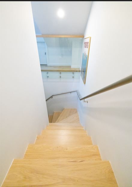 Staircase descending with wooden steps, white walls, and a glass railing.
