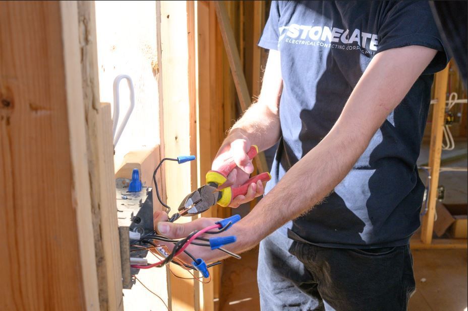 Person wiring electrical box with pliers and wire connectors in a wood-framed wall.