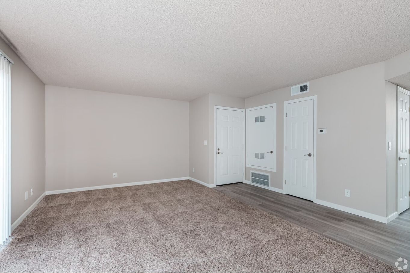 Empty living room with carpet, beige walls, and white doors.