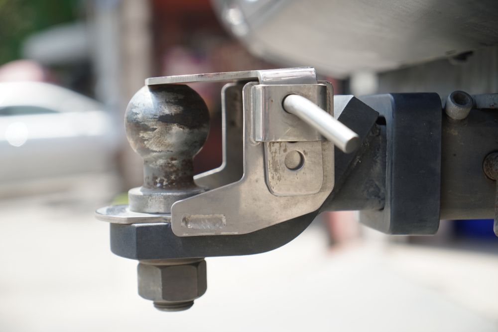 A trailer hitch with a ball and safety latch, attached to a vehicle's bumper. — Jakes Tyres in South Murwillumbah, NSW