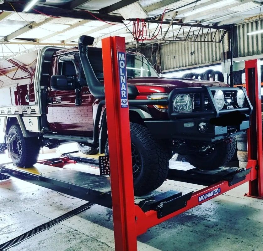 Red truck on a red Molnar lift in a garage, with snorkel and black wheels. — Jakes Tyres in South Murwillumbah, NSW