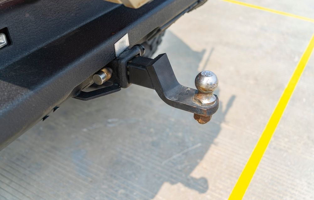 Black trailer hitch attached to a vehicle bumper, with a silver ball hitch.