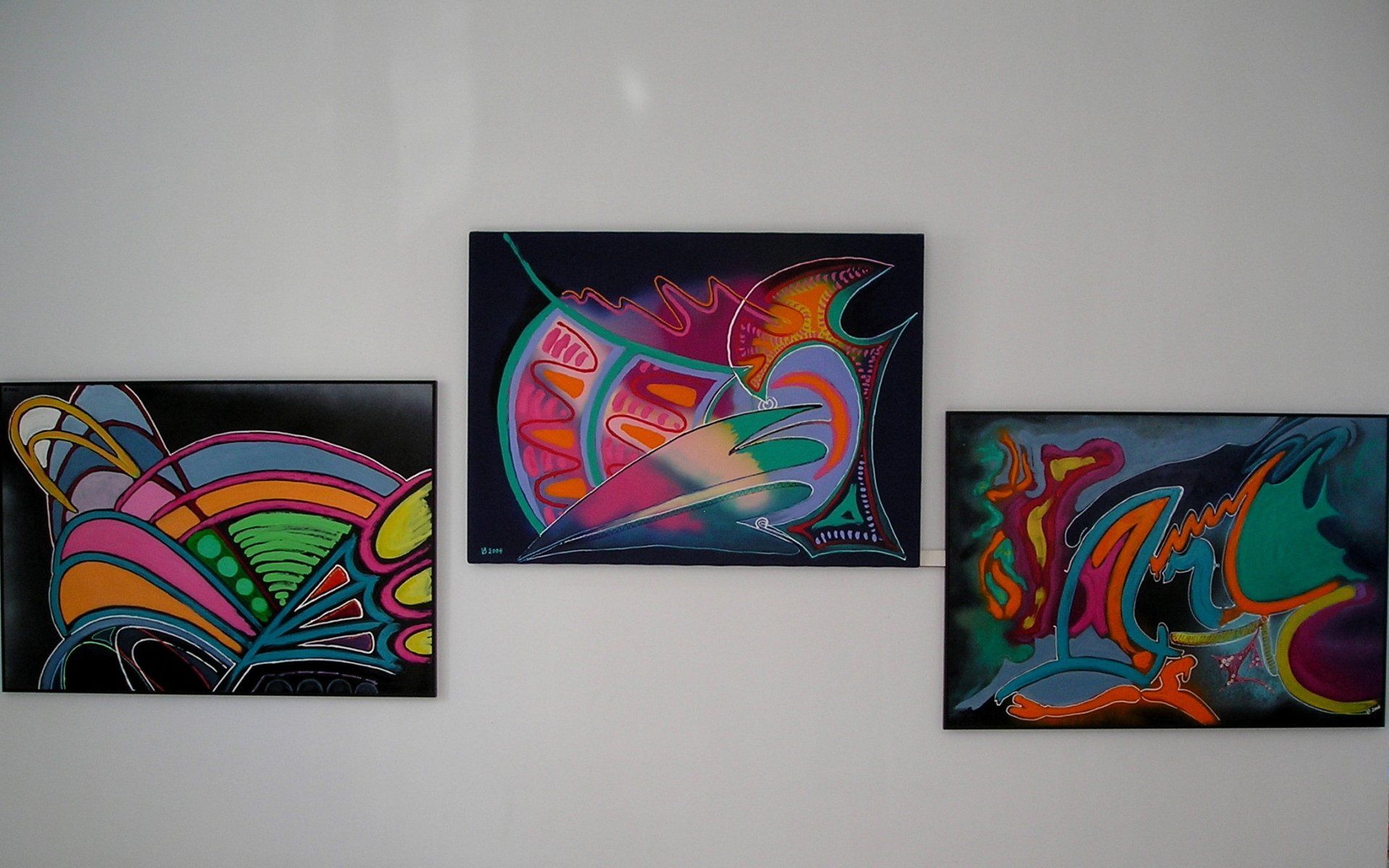 An einer weißen Wand hängen drei bunte Gemälde.