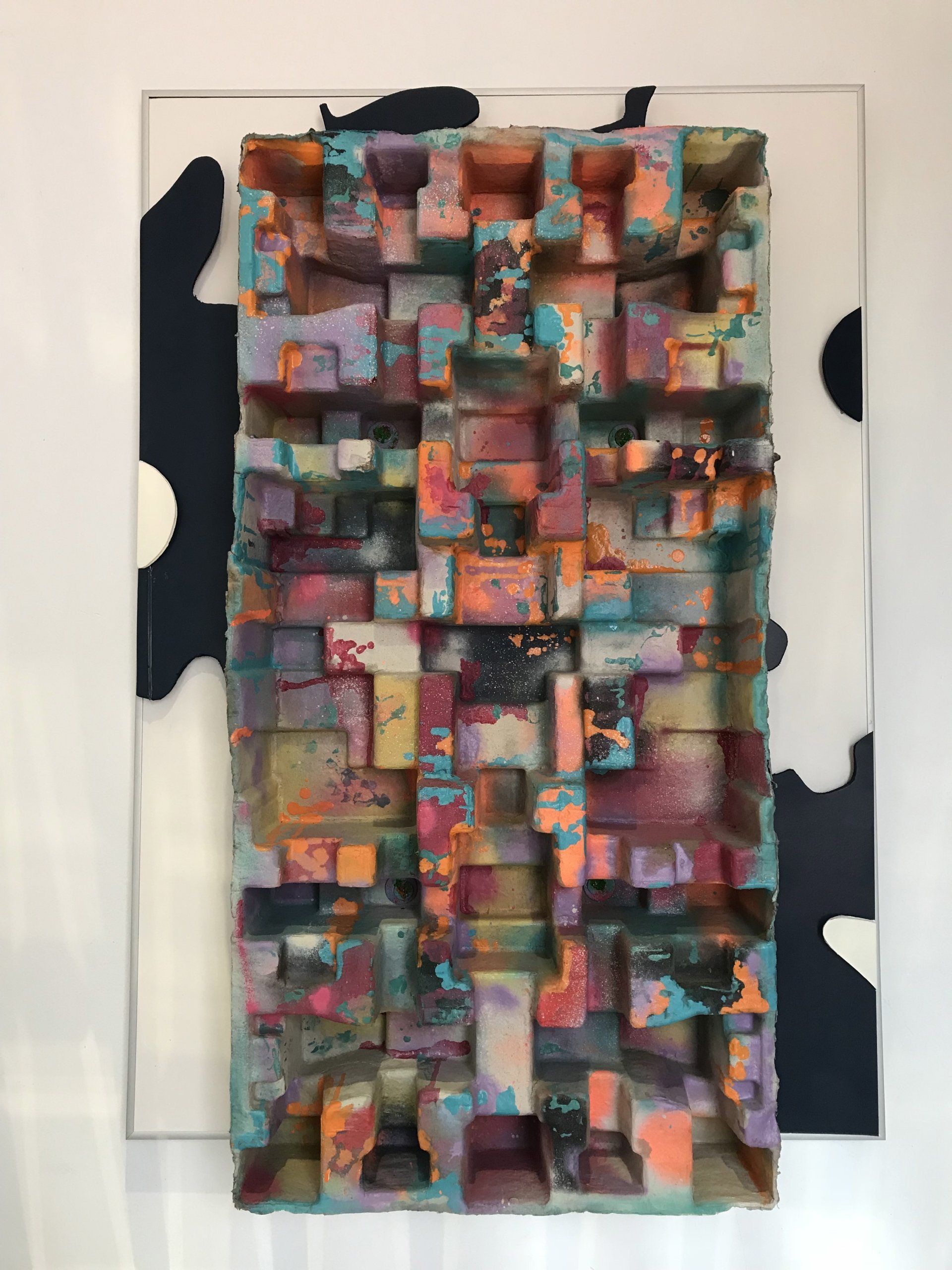 An einer weißen Wand hängt ein buntes Gemälde.