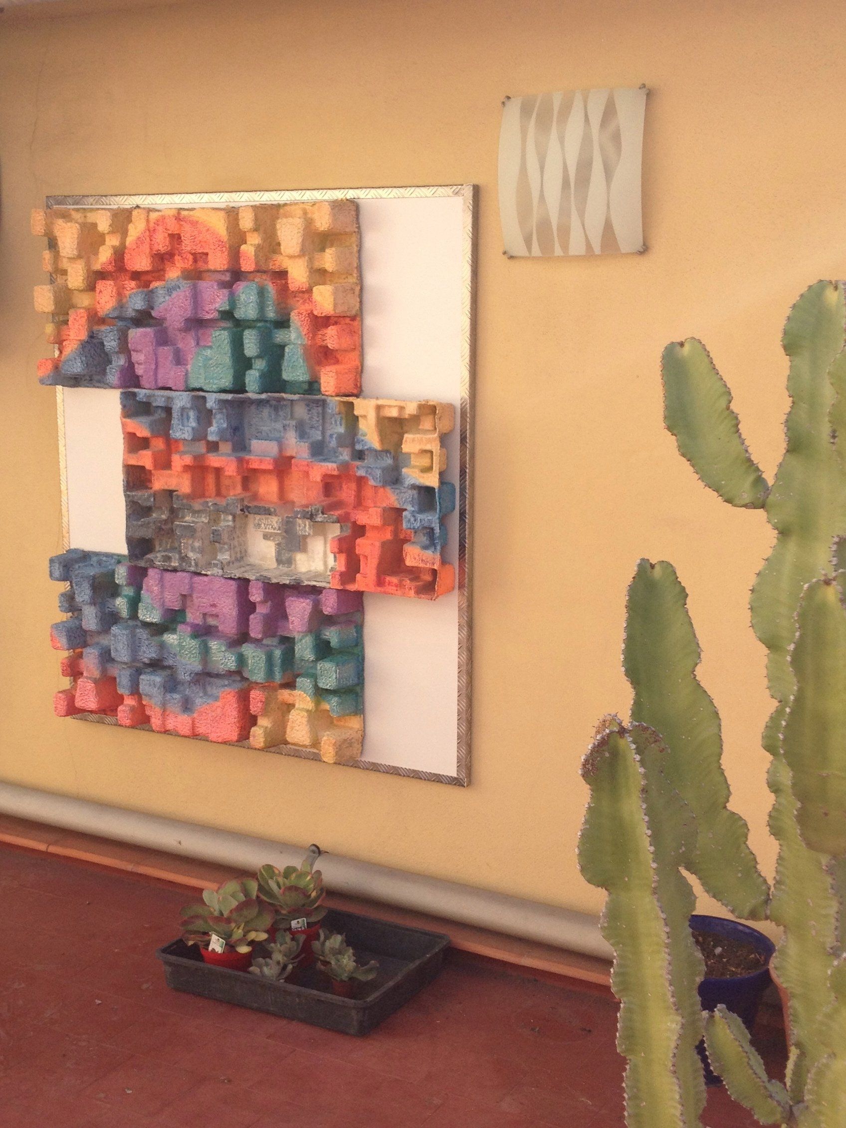 An einer Wand neben einem Kaktus hängt ein farbenfrohes Gemälde.
