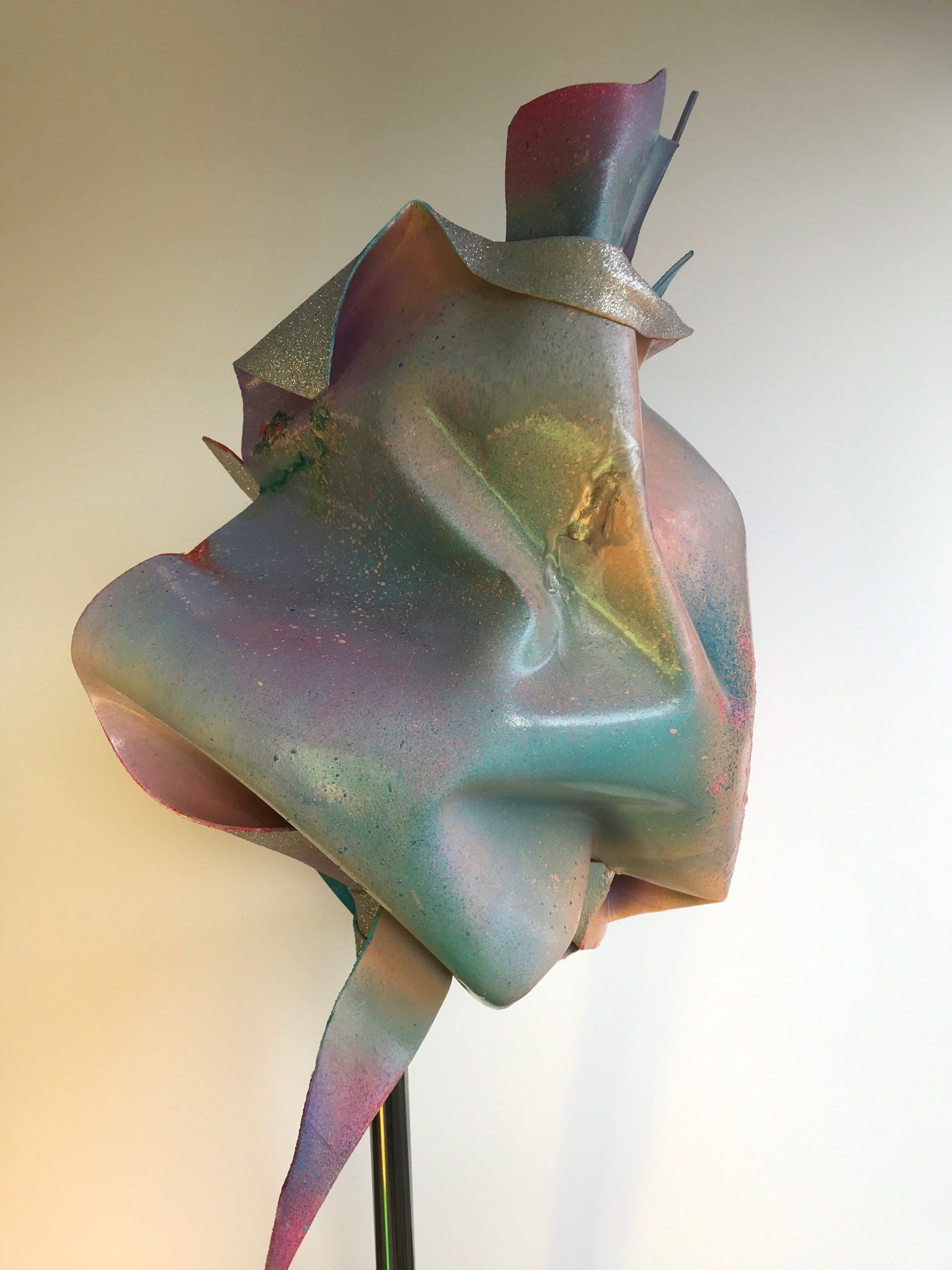 Eine bunte Skulptur sitzt auf einem Ständer vor einer weißen Wand