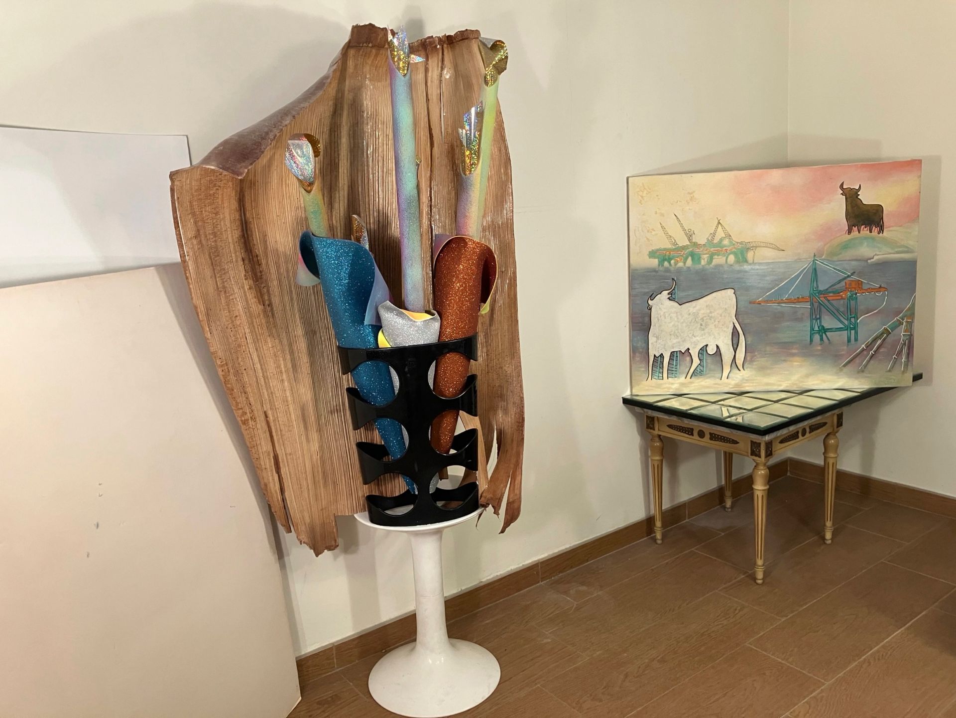 Skulptur mit buntem, herabhängendem Stoff, daneben ein Gemälde auf einem kleinen Tisch.