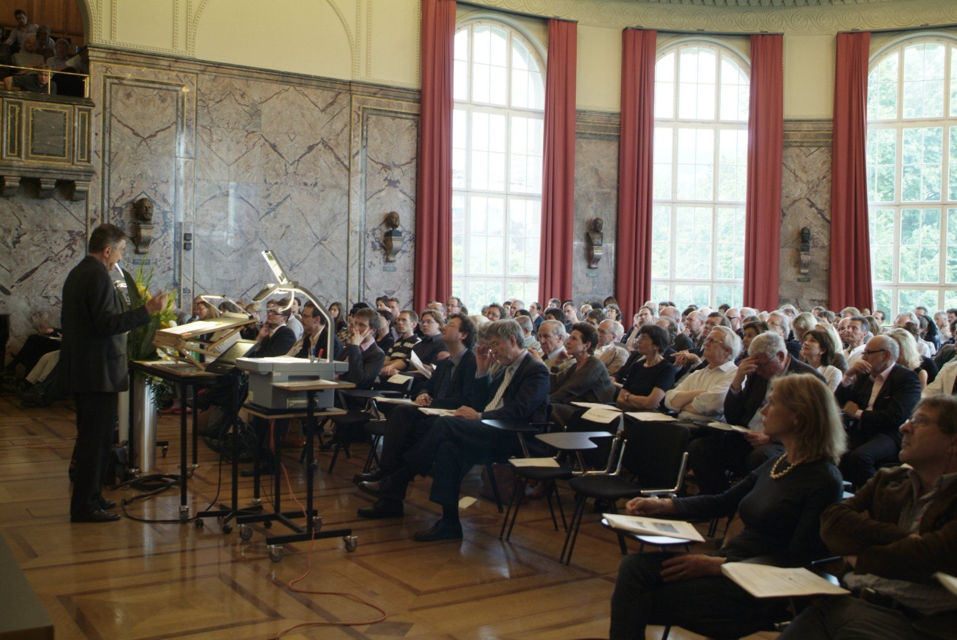 Ein Mann hält vor einer großen Gruppe von Menschen in einem großen Raum eine Präsentation.