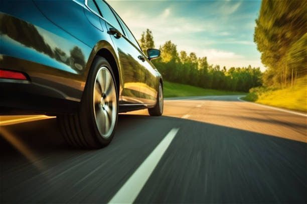 A car is driving down a road with trees in the background.