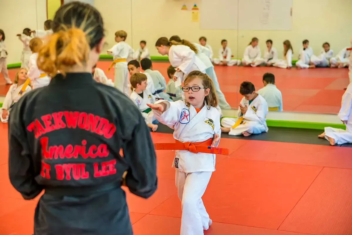 Girl in orange belt practicing karate under instruction in a dojo