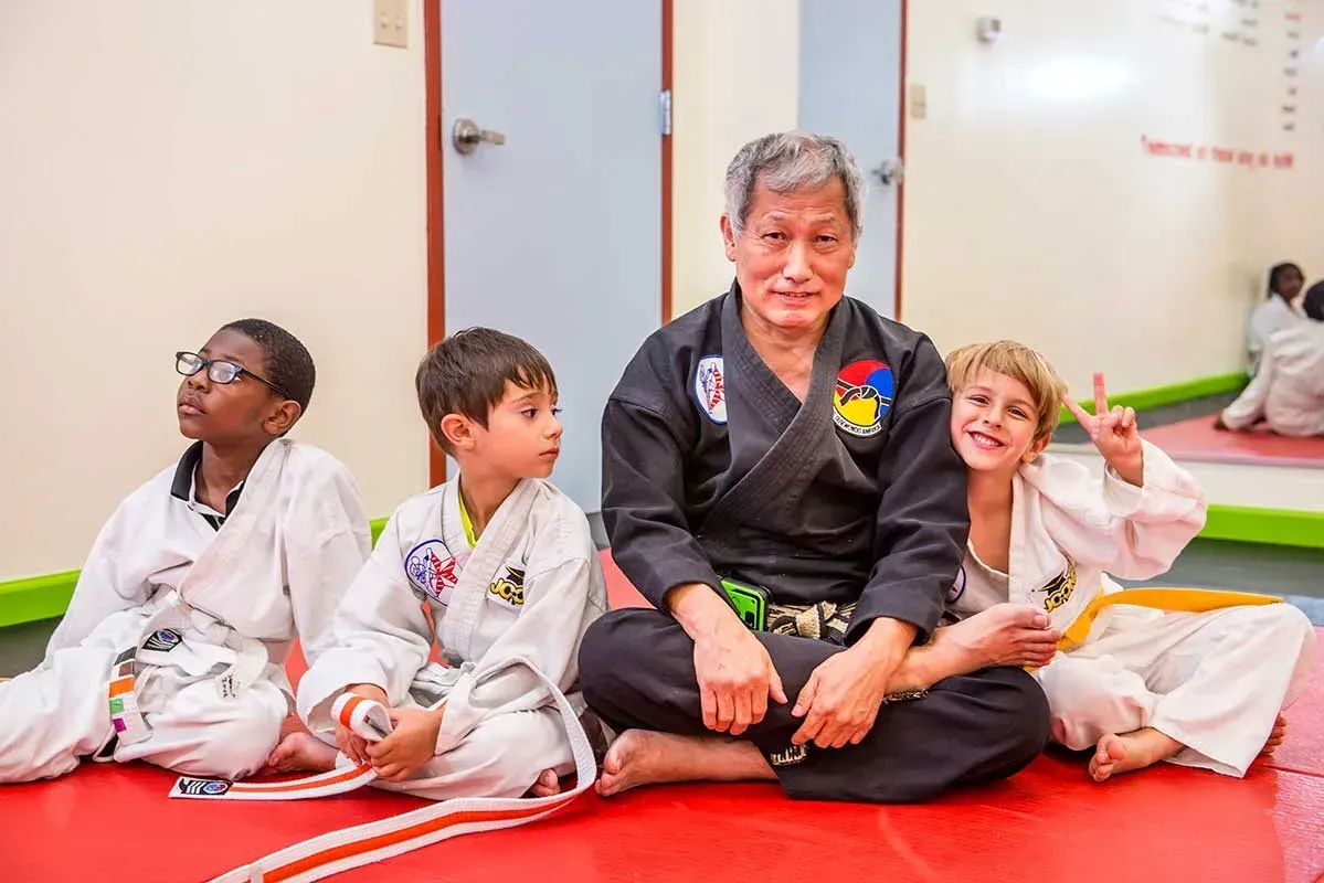 Martial arts instructor sits with three children on a red mat