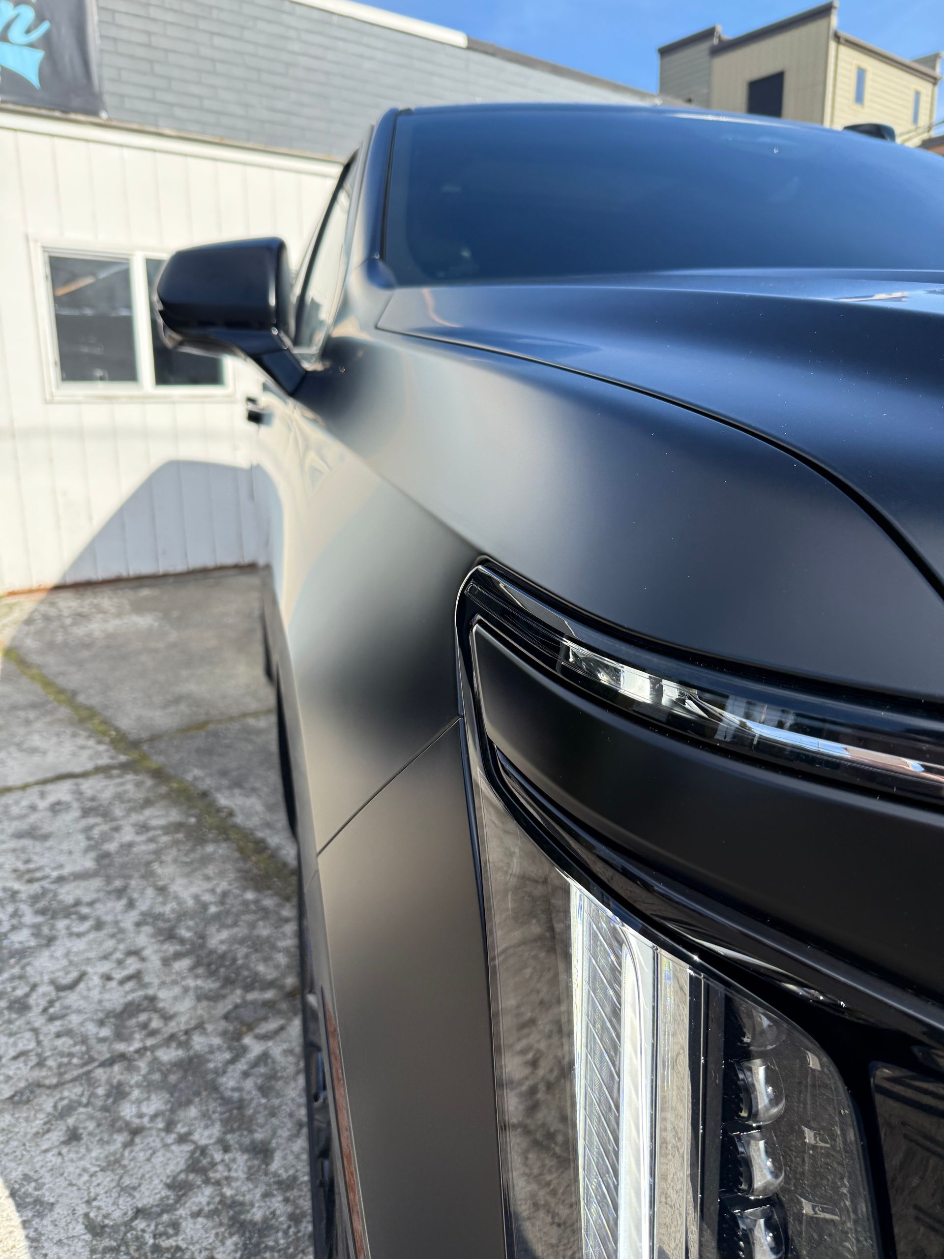 Black car parked beside a white house, close-up of front headlight and side mirror.