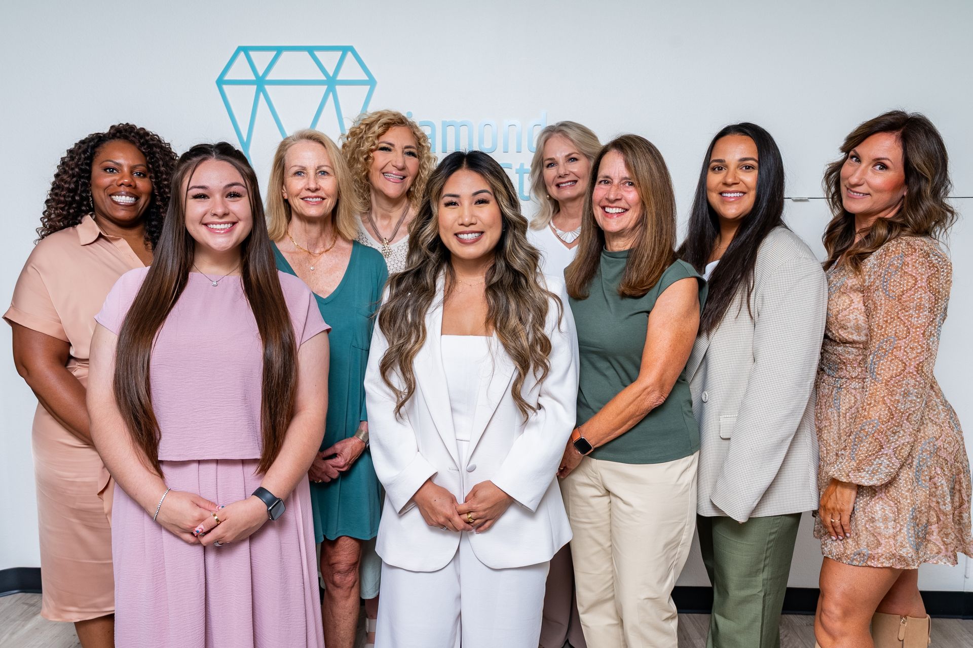 Group of diverse women smiling in front of a logo, wearing business casual attire.