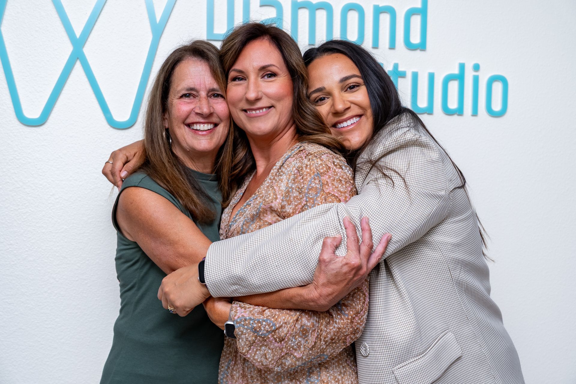 Three smiling women embracing in front of a blue studio sign.