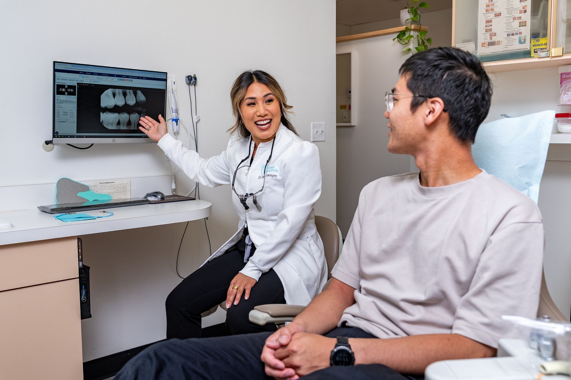 Dentist pointing to x-ray on screen, explaining to male patient in dental chair; smiles, clinic.