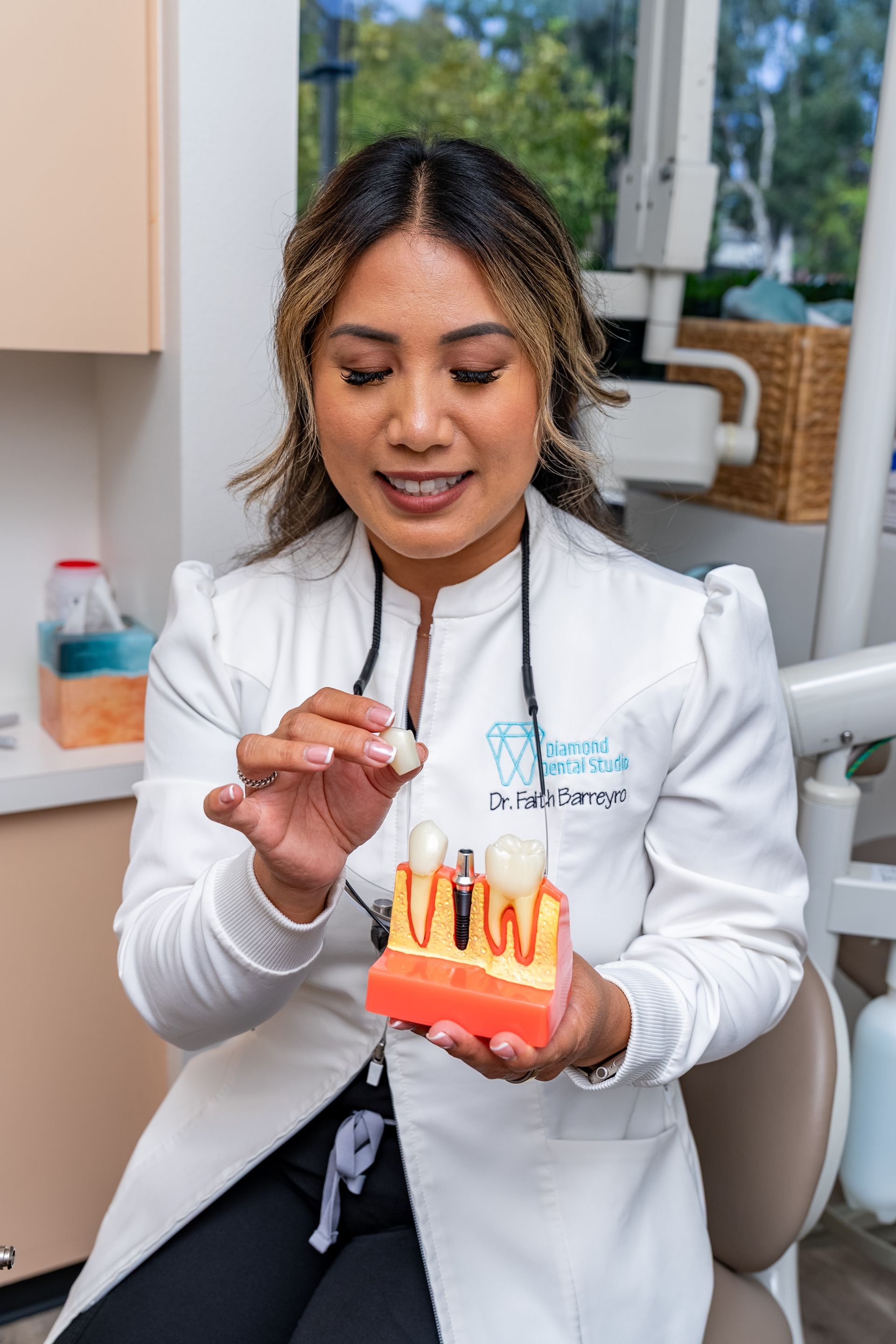 Dentist demonstrating a tooth model; indoors, smiling, holding a small object.