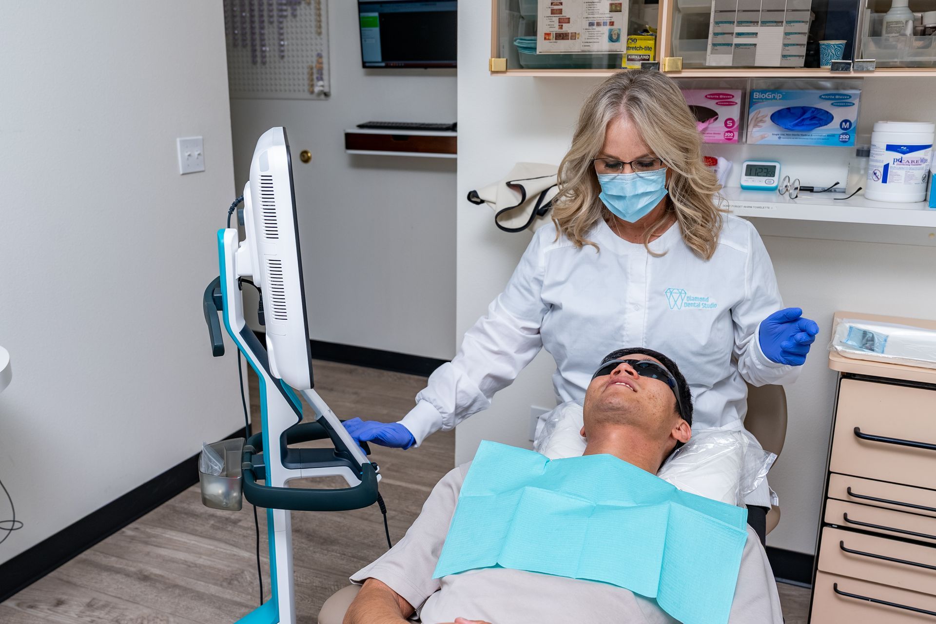 Dentist examining patient in office; both wearing masks and gloves.