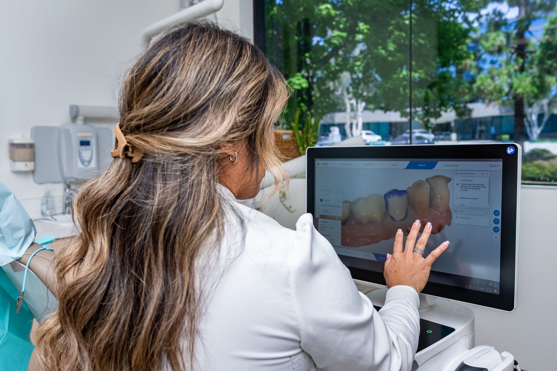 Dentist reviews 3D tooth model on screen in dental office, pointing with finger.