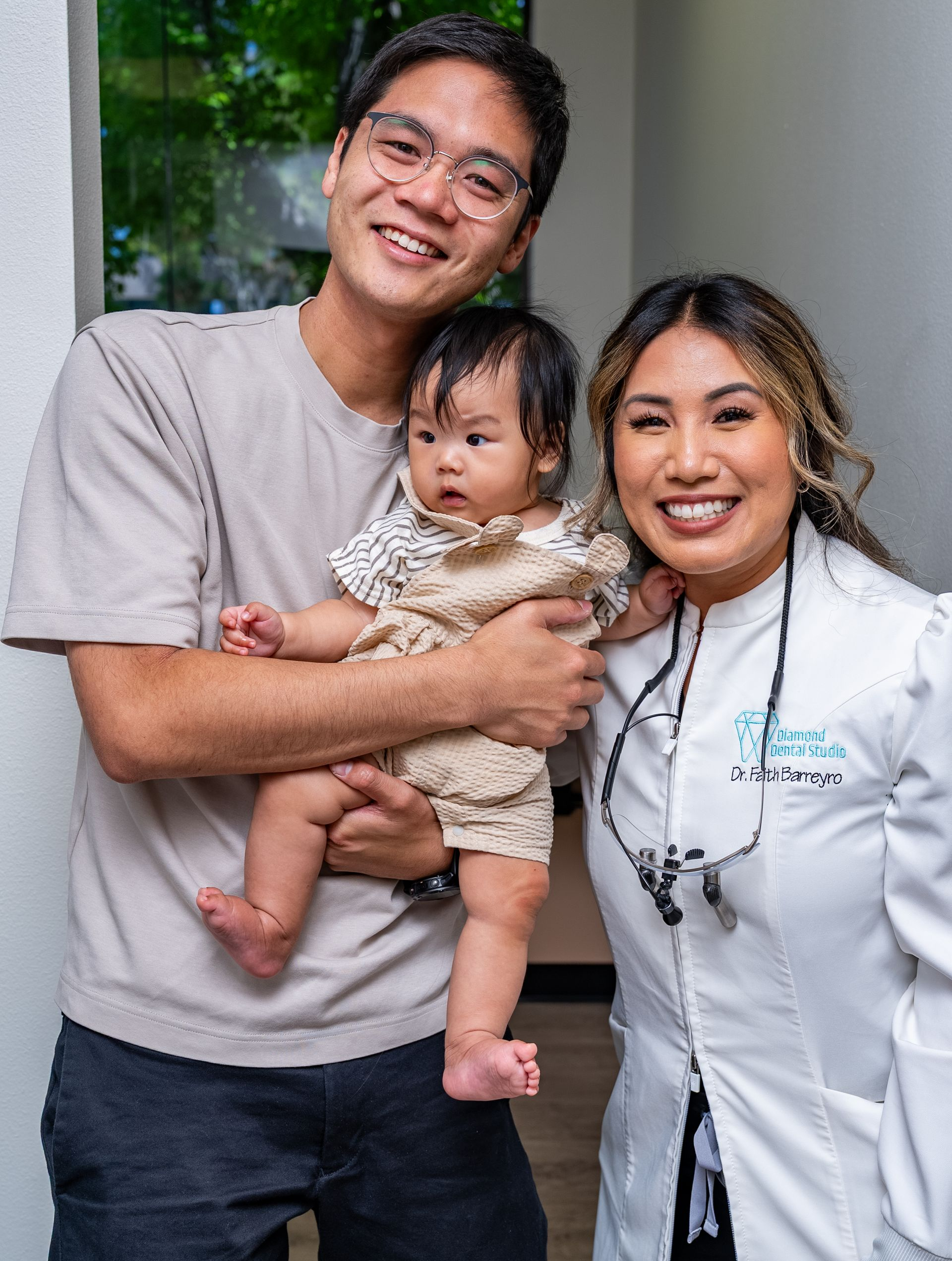 Man holds baby while smiling with woman in white coat.