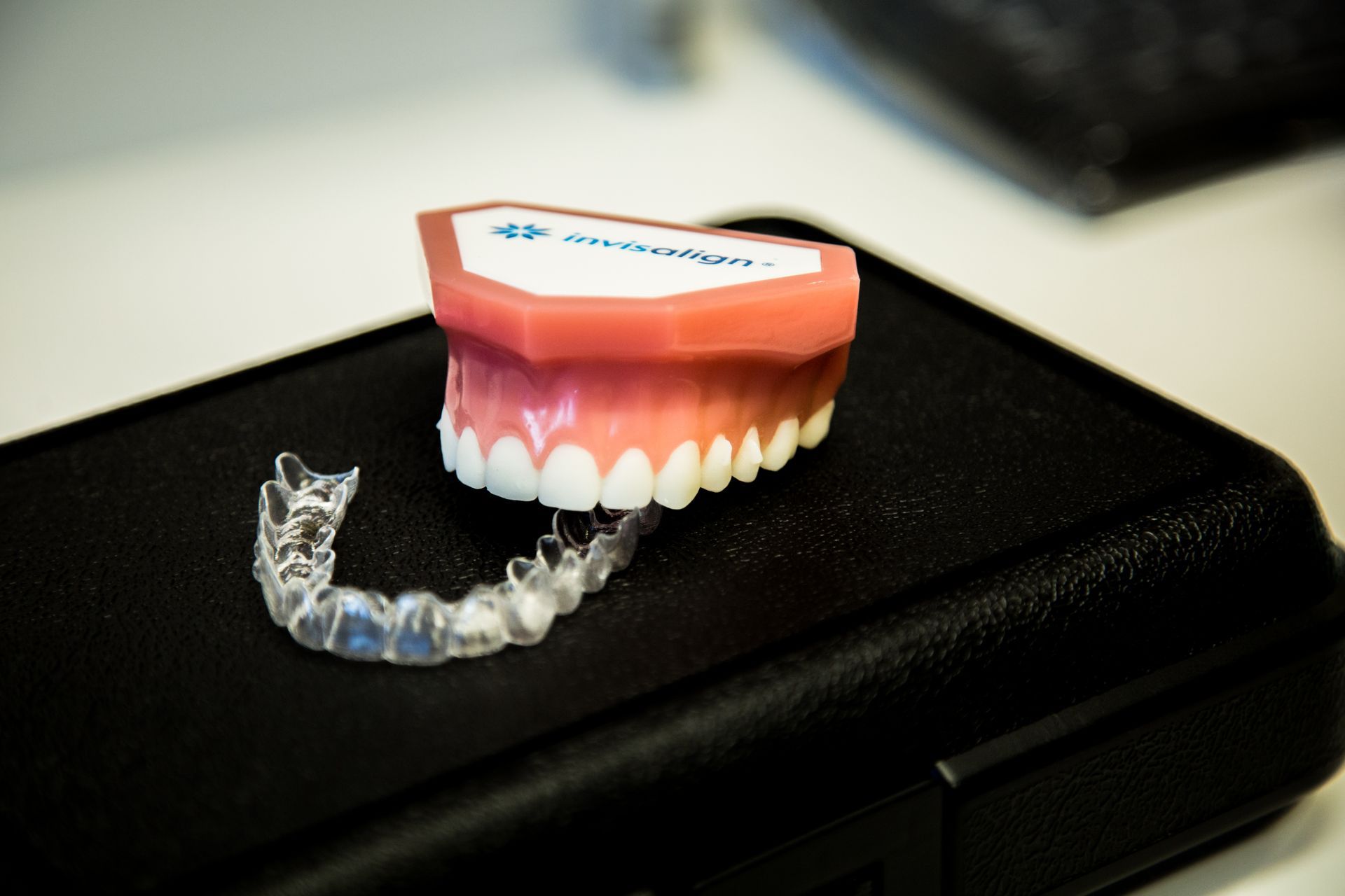 Clear Invisalign aligner next to a model of teeth on a black case.