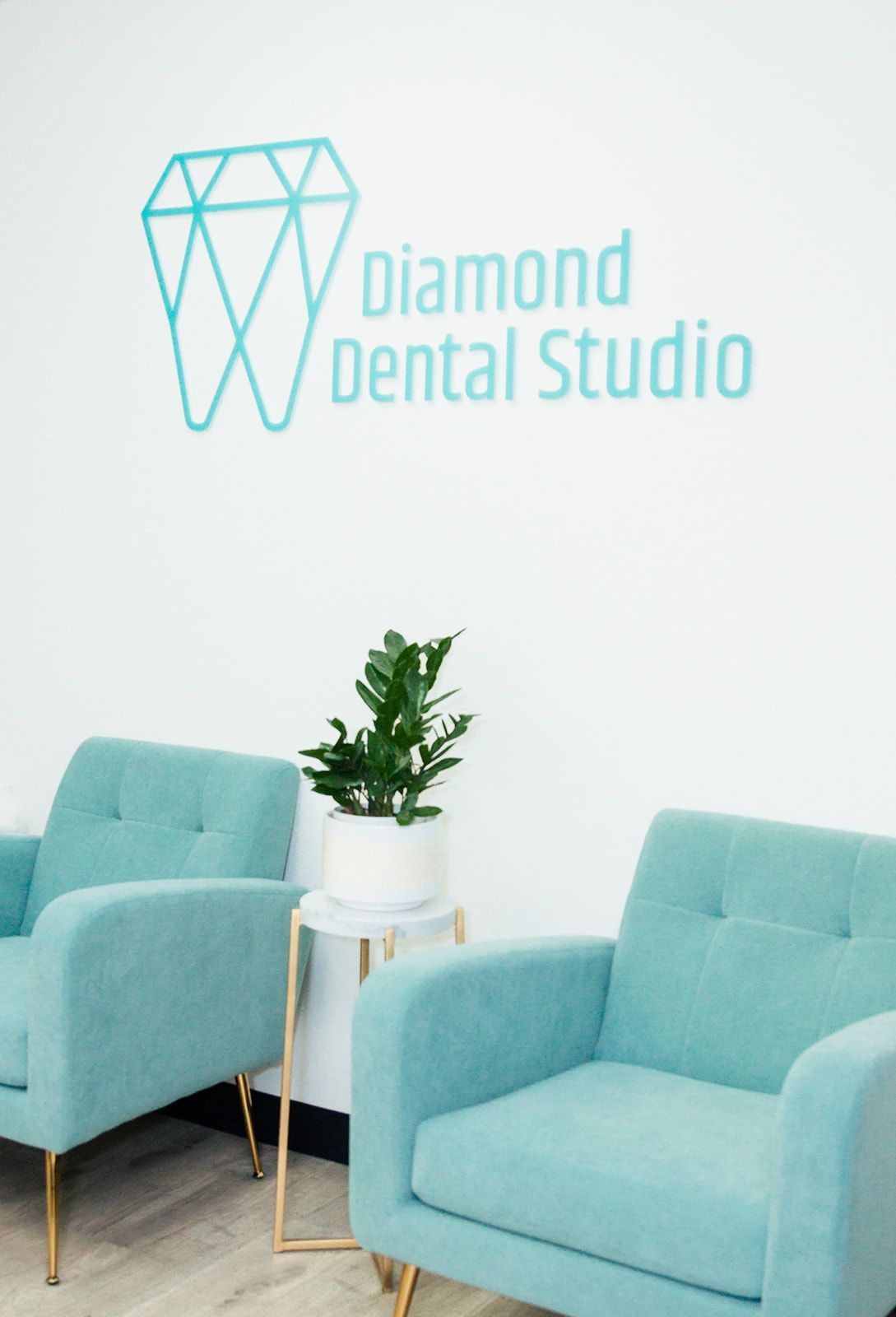 Two teal armchairs in a dental studio, with a plant on a side table; a diamond logo and text above.