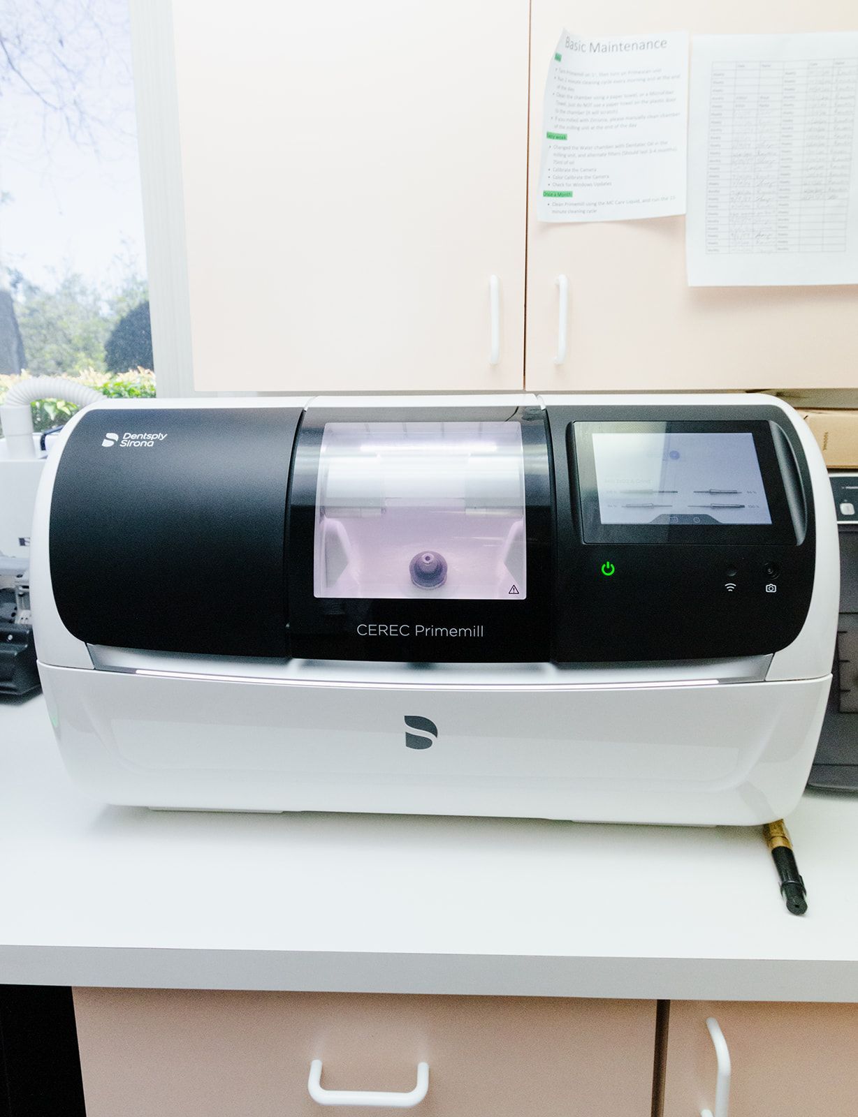A dental milling machine in a doctor's office. Black and white, with a ceramic dental restoration inside.