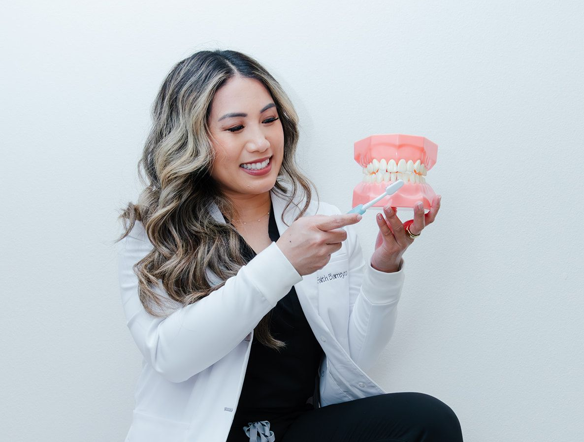 Dentist demonstrating brushing technique with a model of teeth; woman smiles, points with brush.