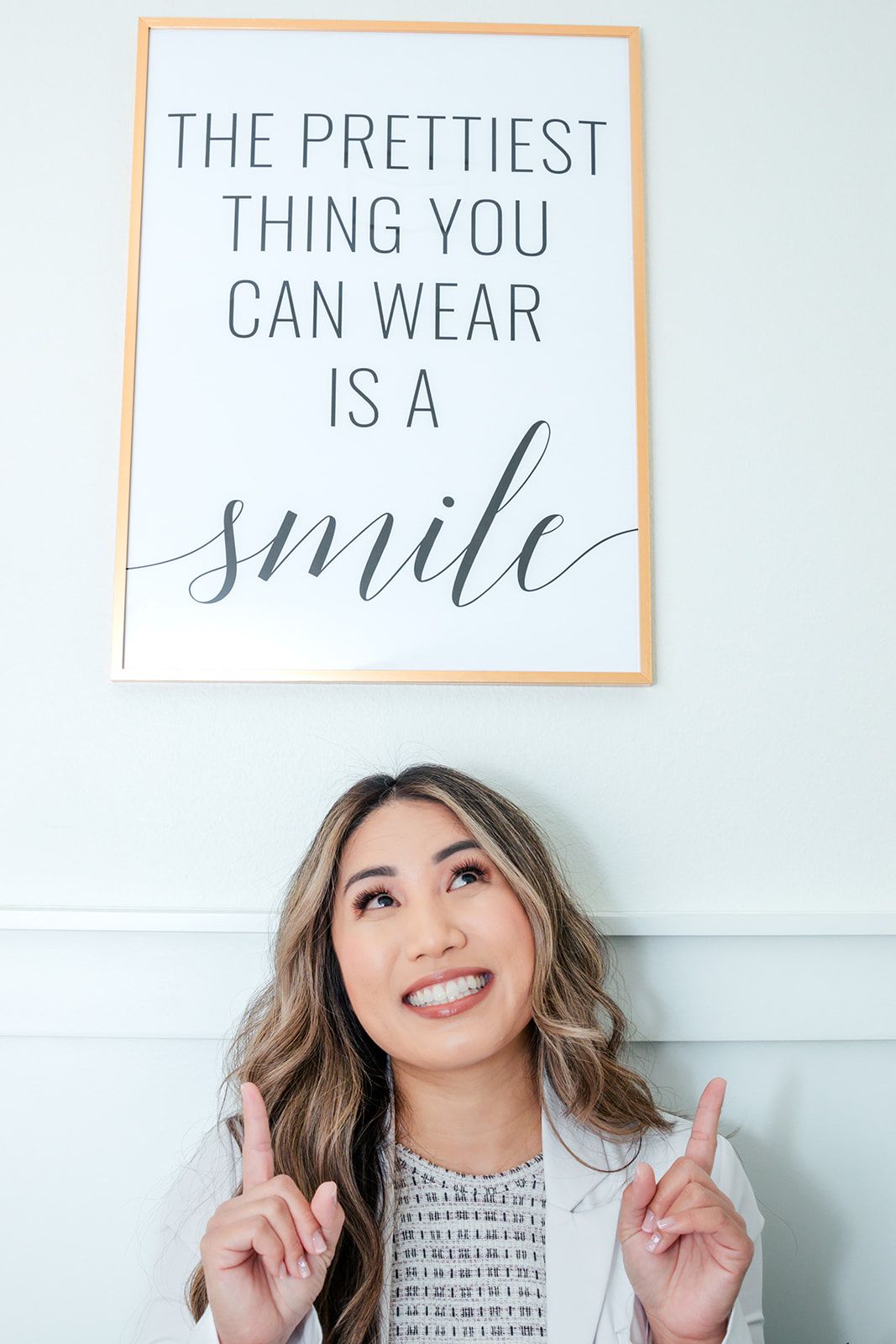 Woman smiling, pointing upwards, below a framed sign: